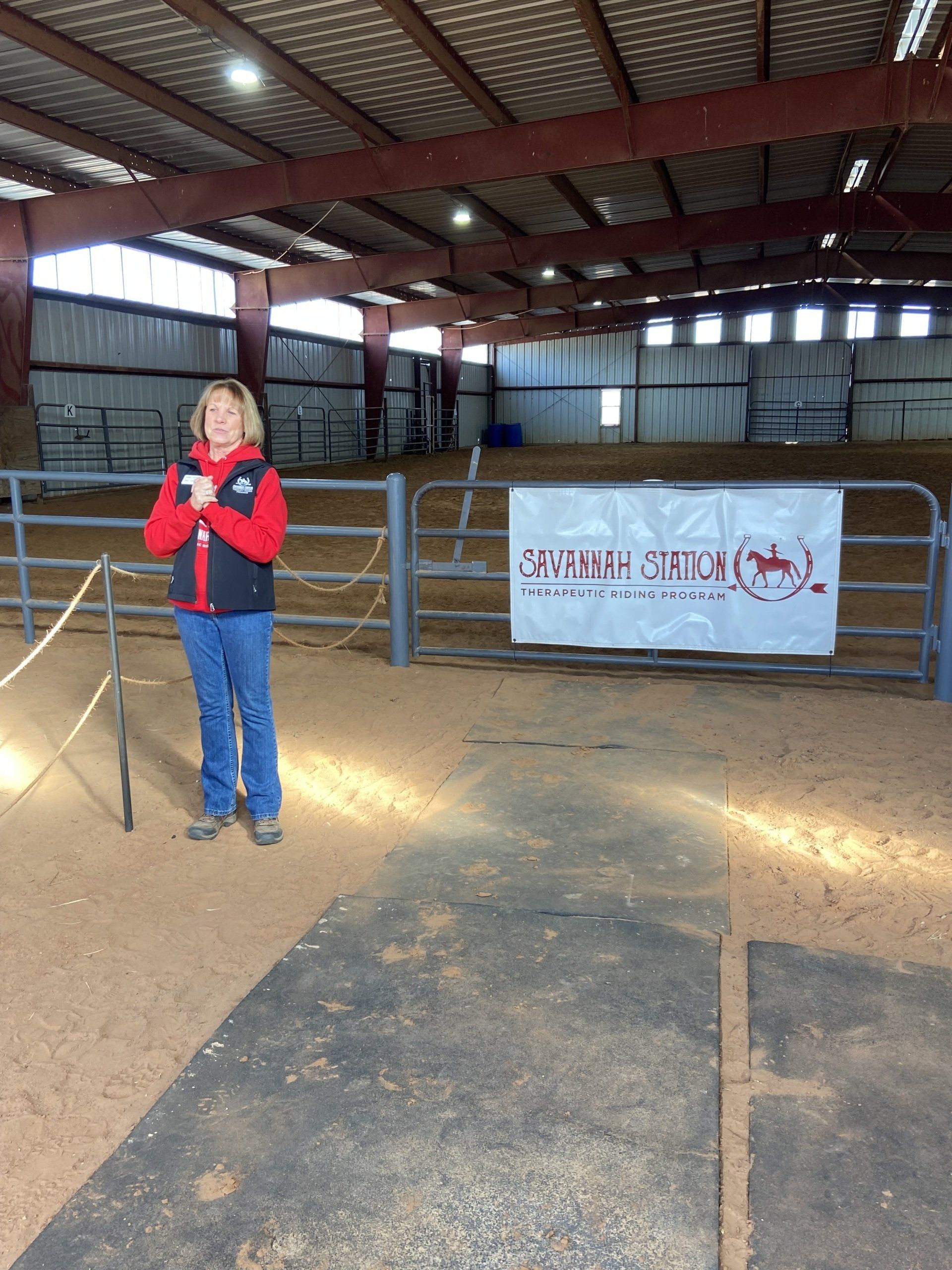 A woman stands in front of a fence with a sign that says ' saddle broncs ' on it