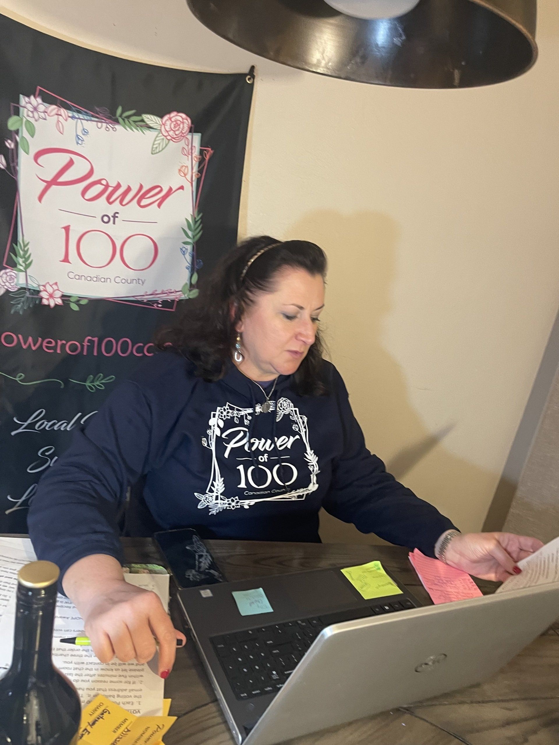 A woman wearing a power of 100 shirt is using a laptop computer.