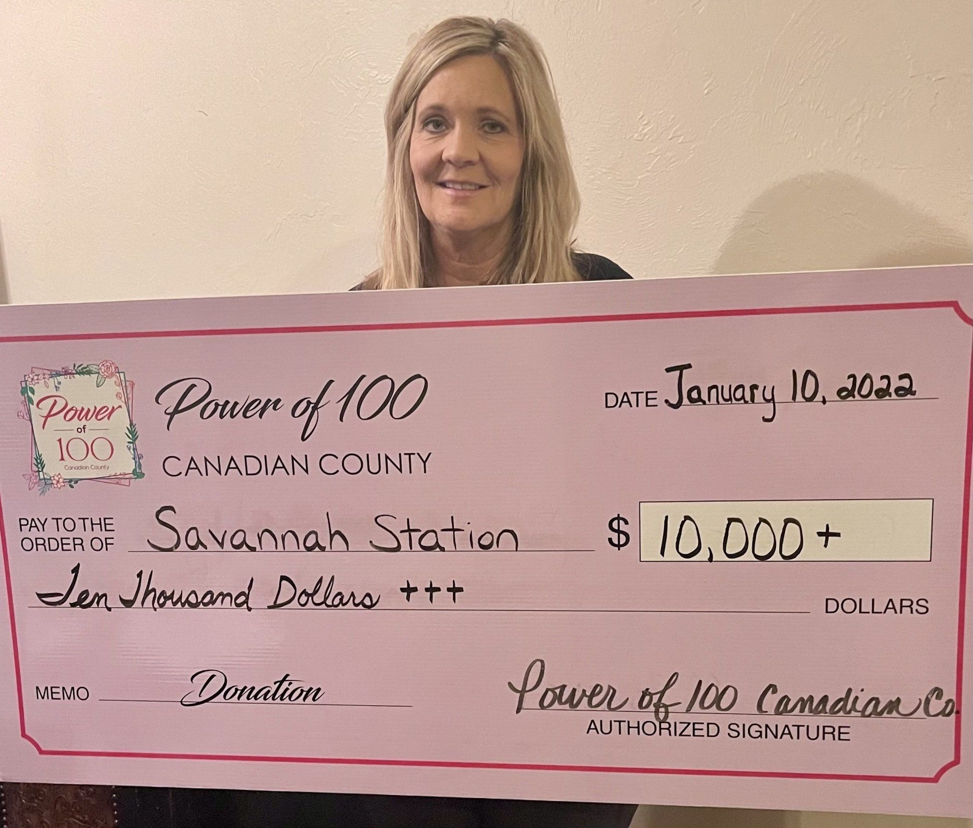 A woman is holding a pink check that says power of 100 canadian county