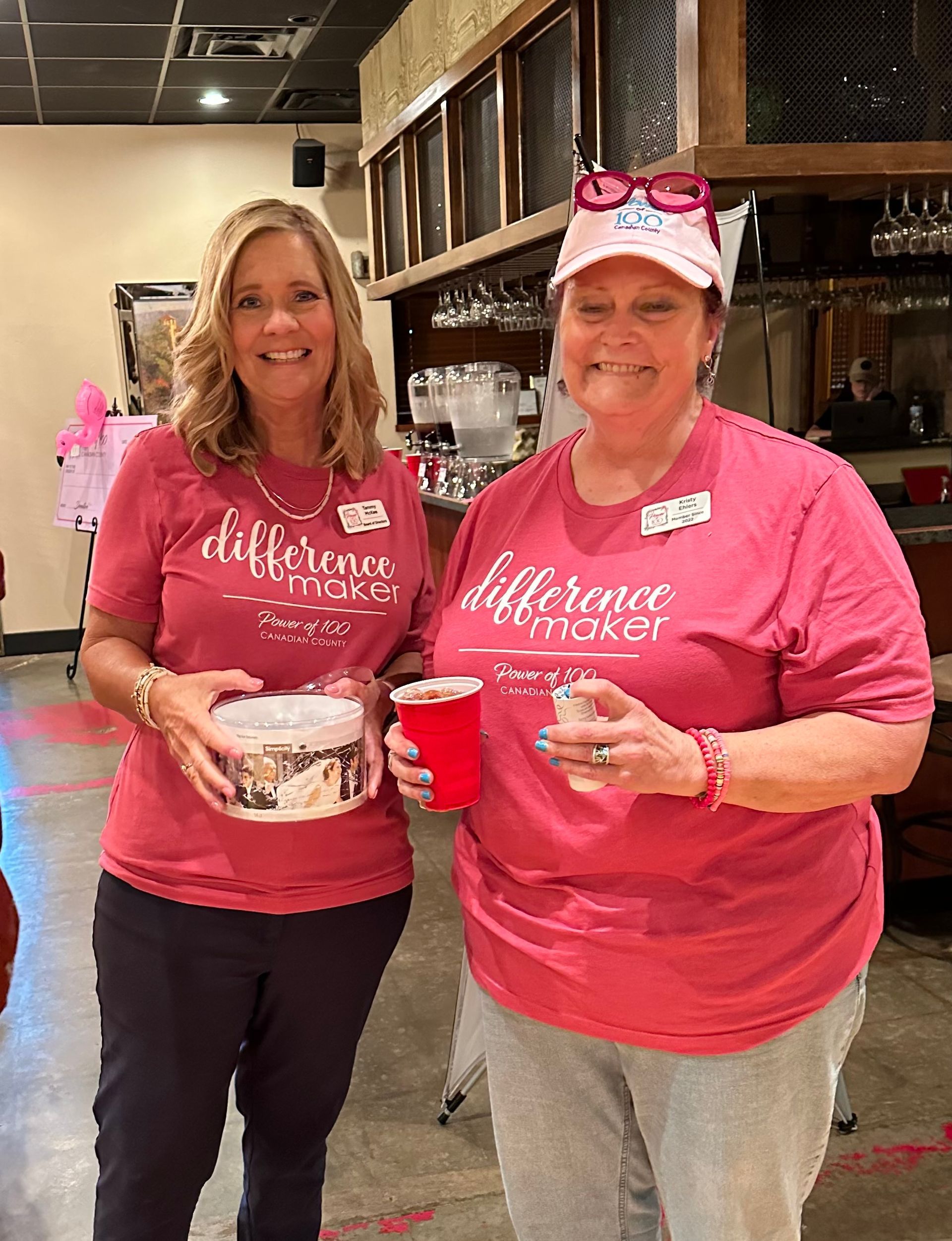 Two women in pink shirts are standing next to each other in a restaurant.