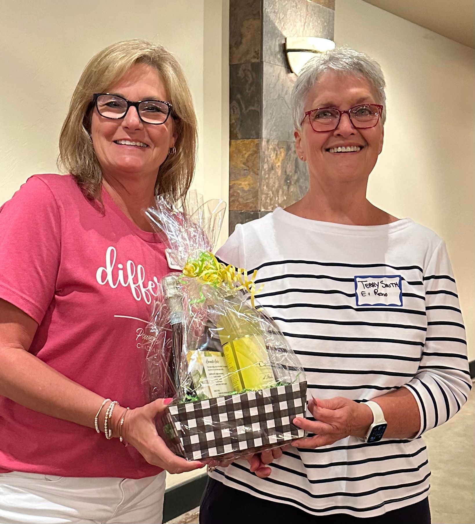 Two women are standing next to each other holding a gift basket.
