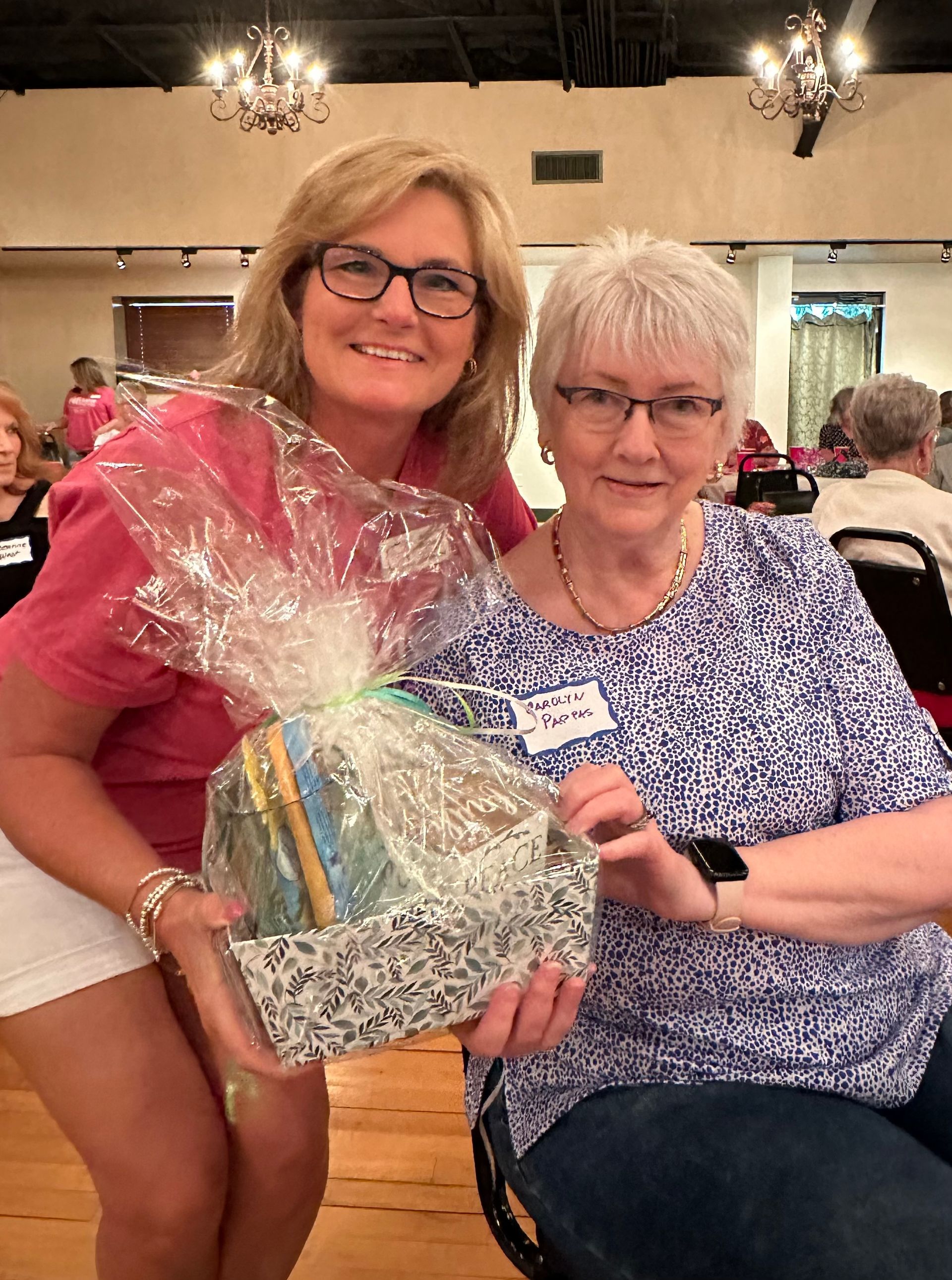 Two women are posing for a picture while holding a gift basket.