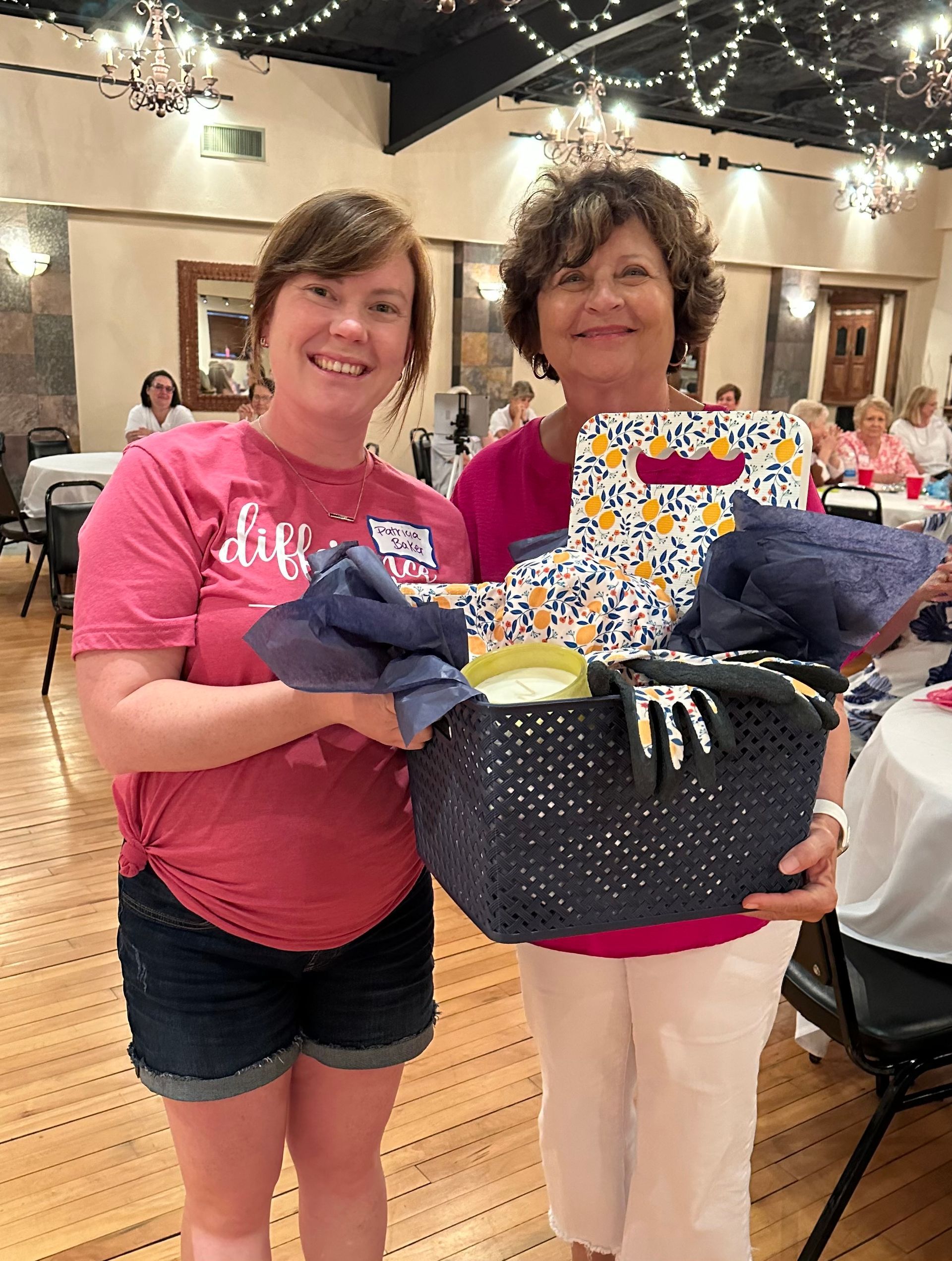 Two women are standing next to each other holding a basket.