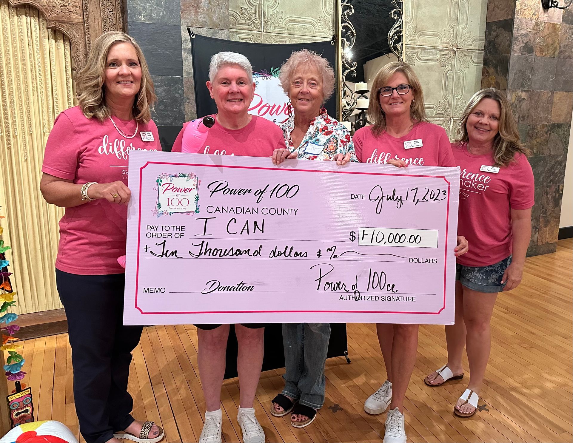 A group of women in pink shirts are holding a large check.