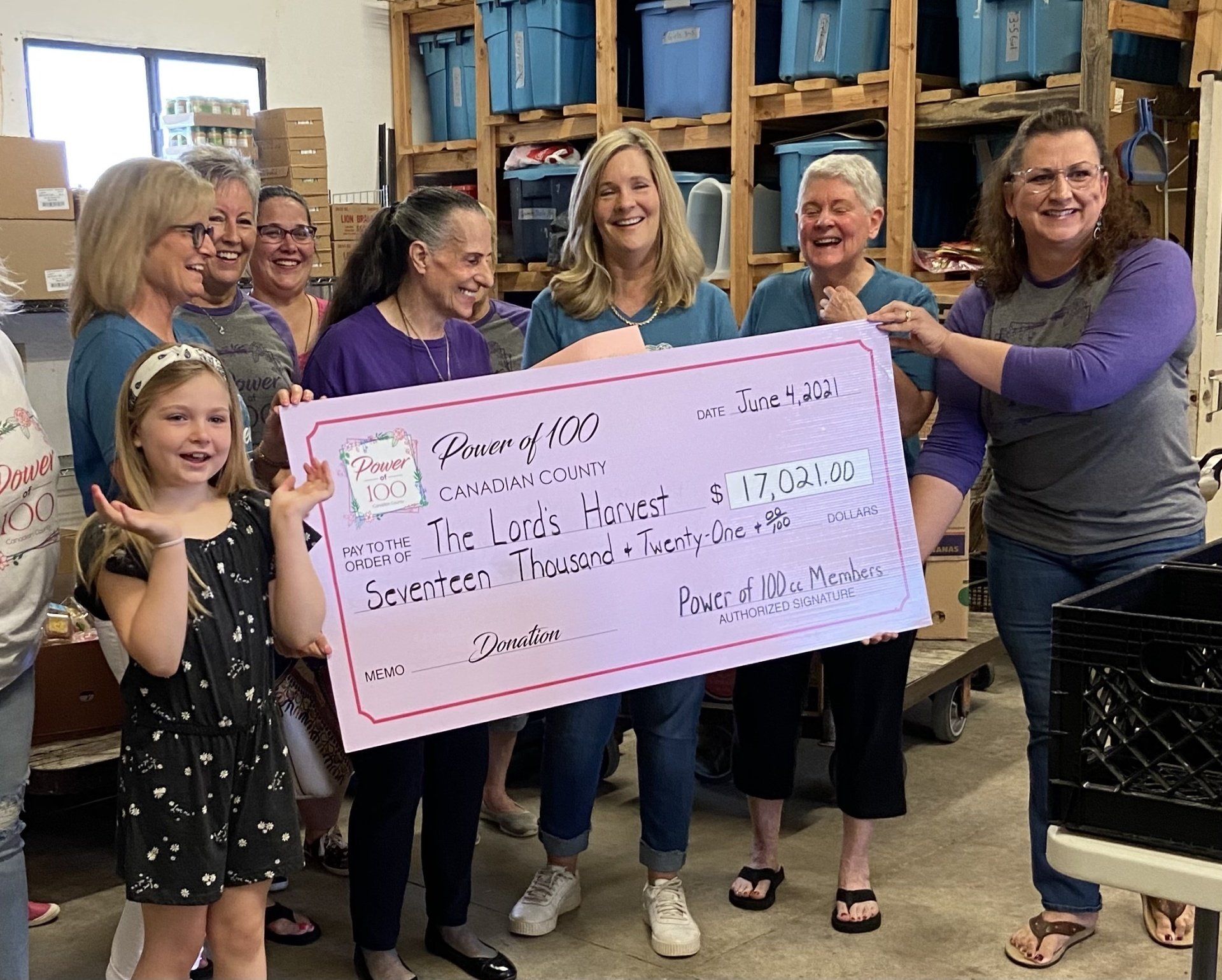 A group of women are holding a large check in a warehouse.