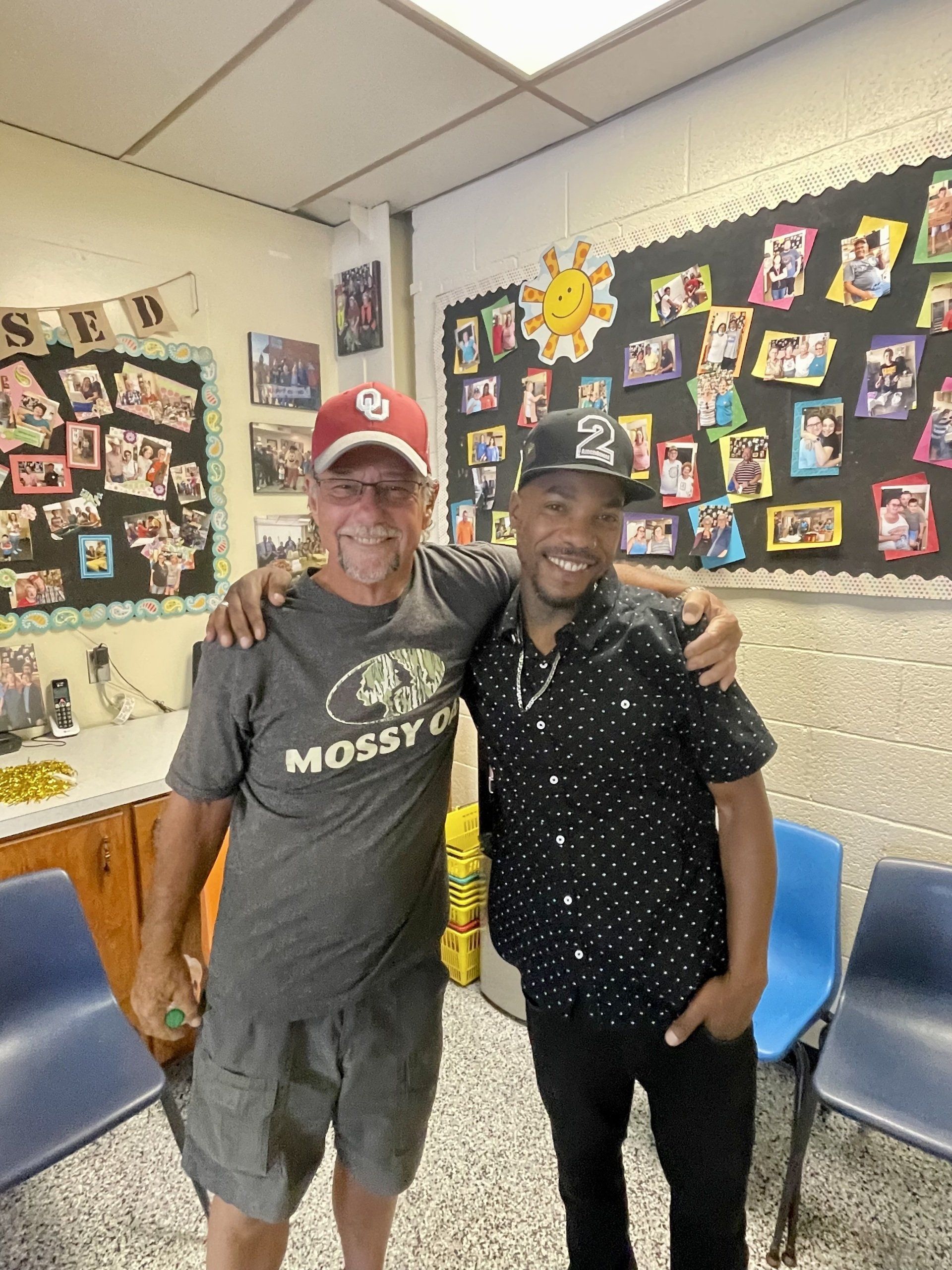 Two men are posing for a picture in a room with pictures on the wall.