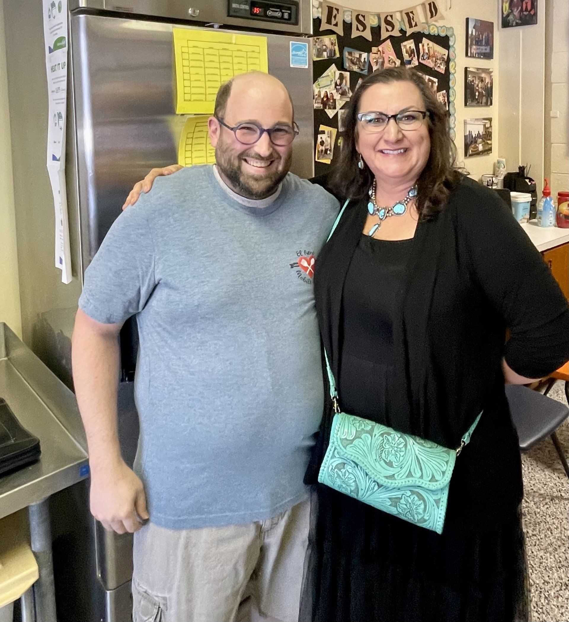 A man and a woman are posing for a picture in front of a refrigerator
