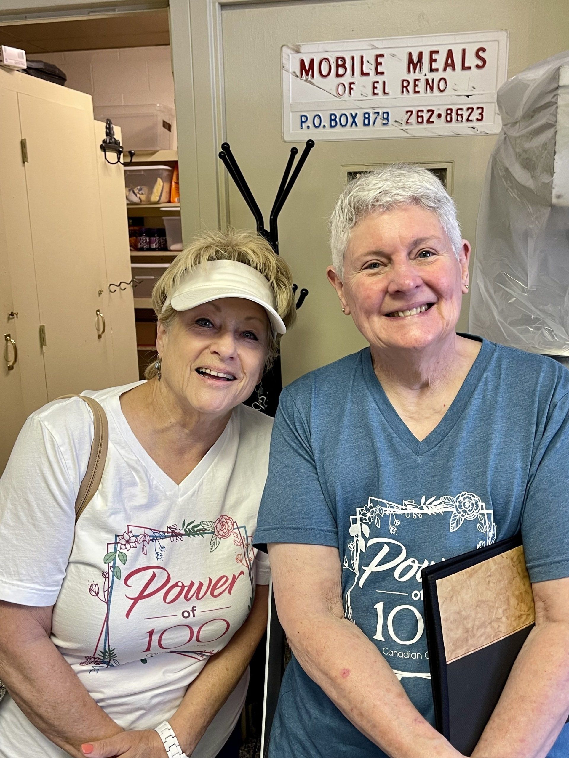 Two women are posing for a picture in front of a sign that says mobile meals