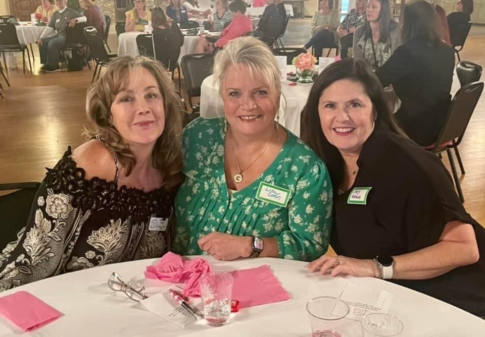 Three women are sitting at a table posing for a picture.