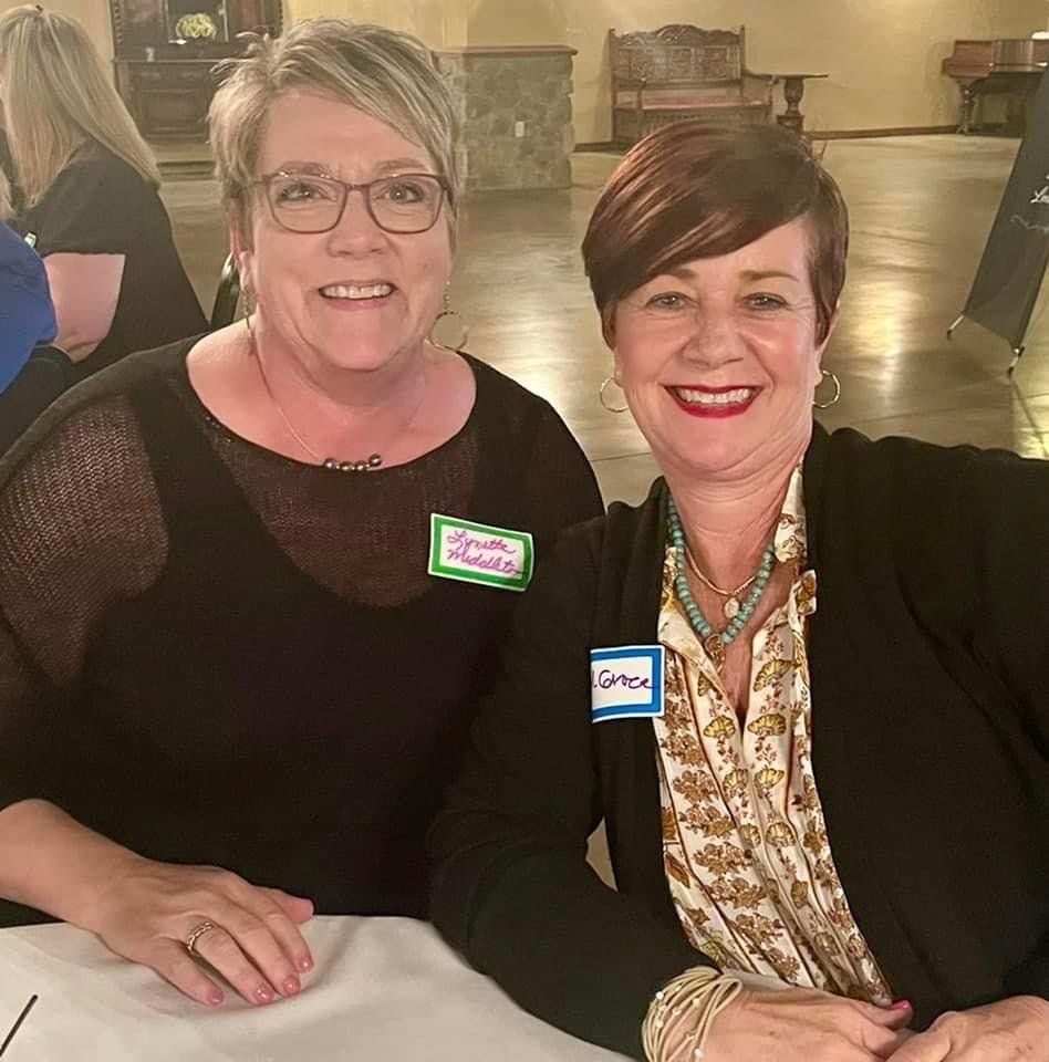 Two women are sitting at a table and smiling for the camera