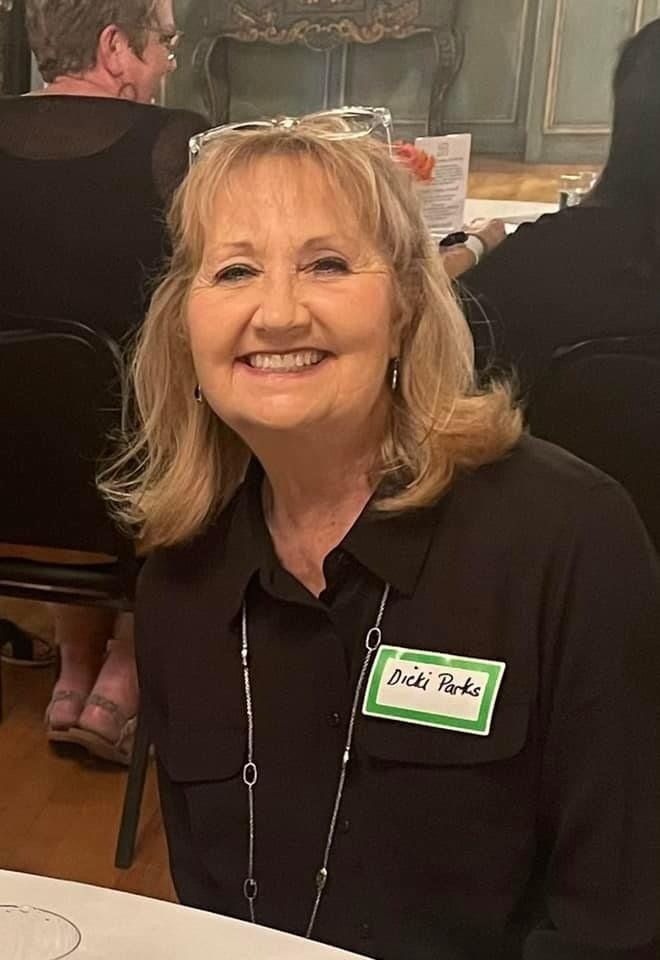 A woman wearing a name tag is smiling while sitting at a table.