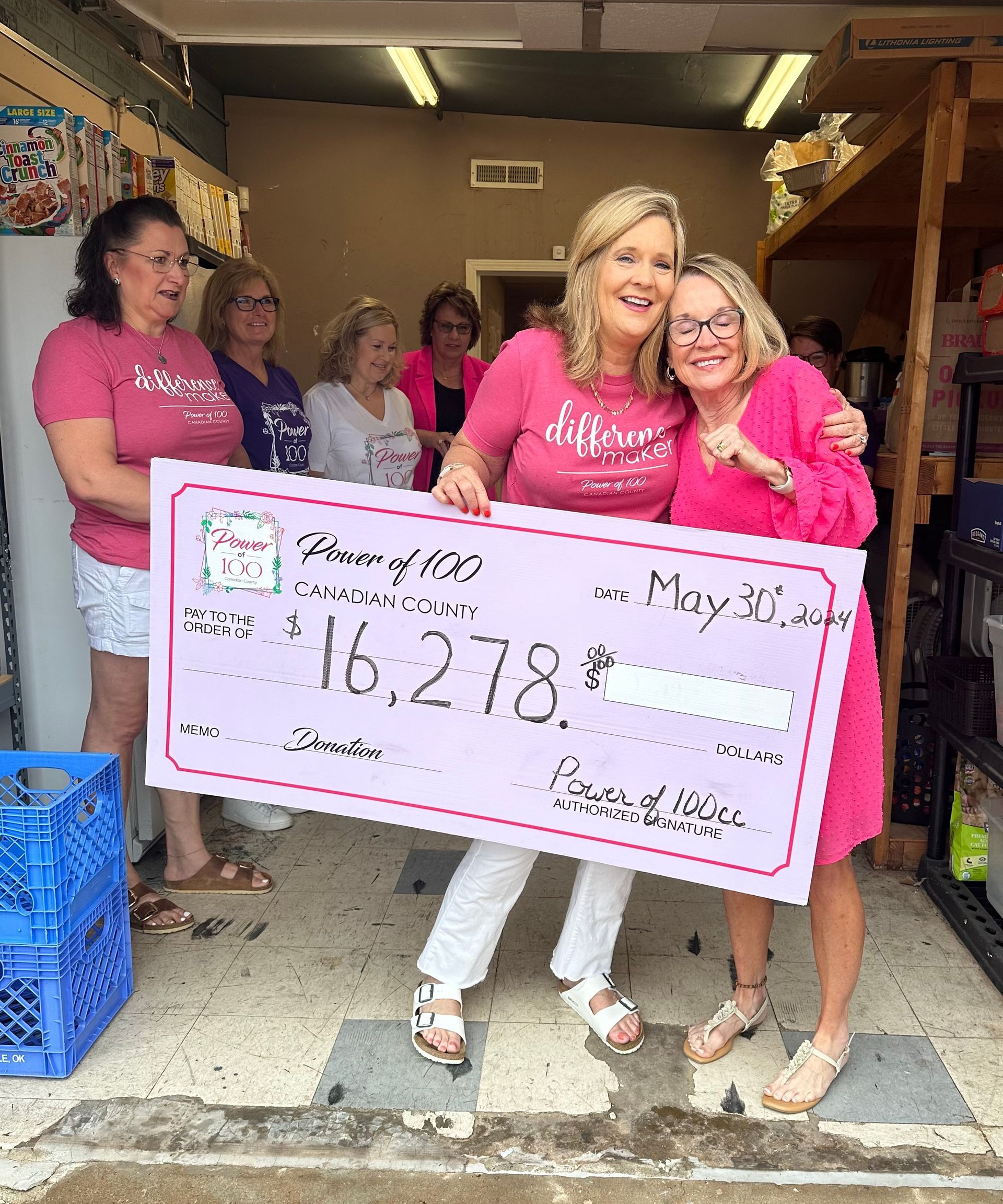 A group of women are standing next to each other holding a large pink check.