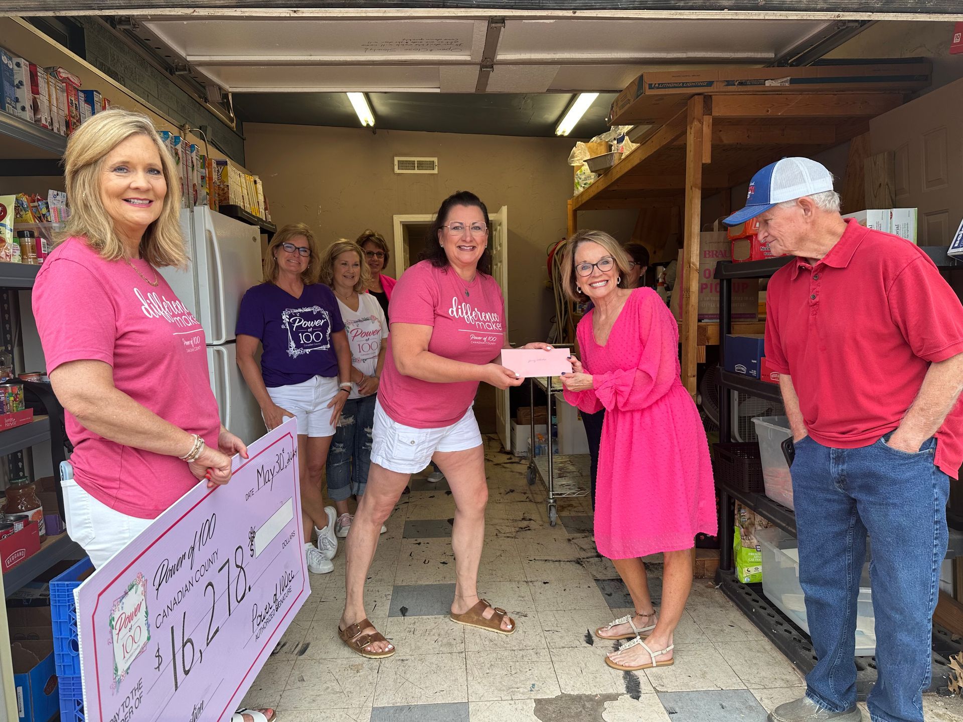 A group of women are standing in a garage holding a large pink check.