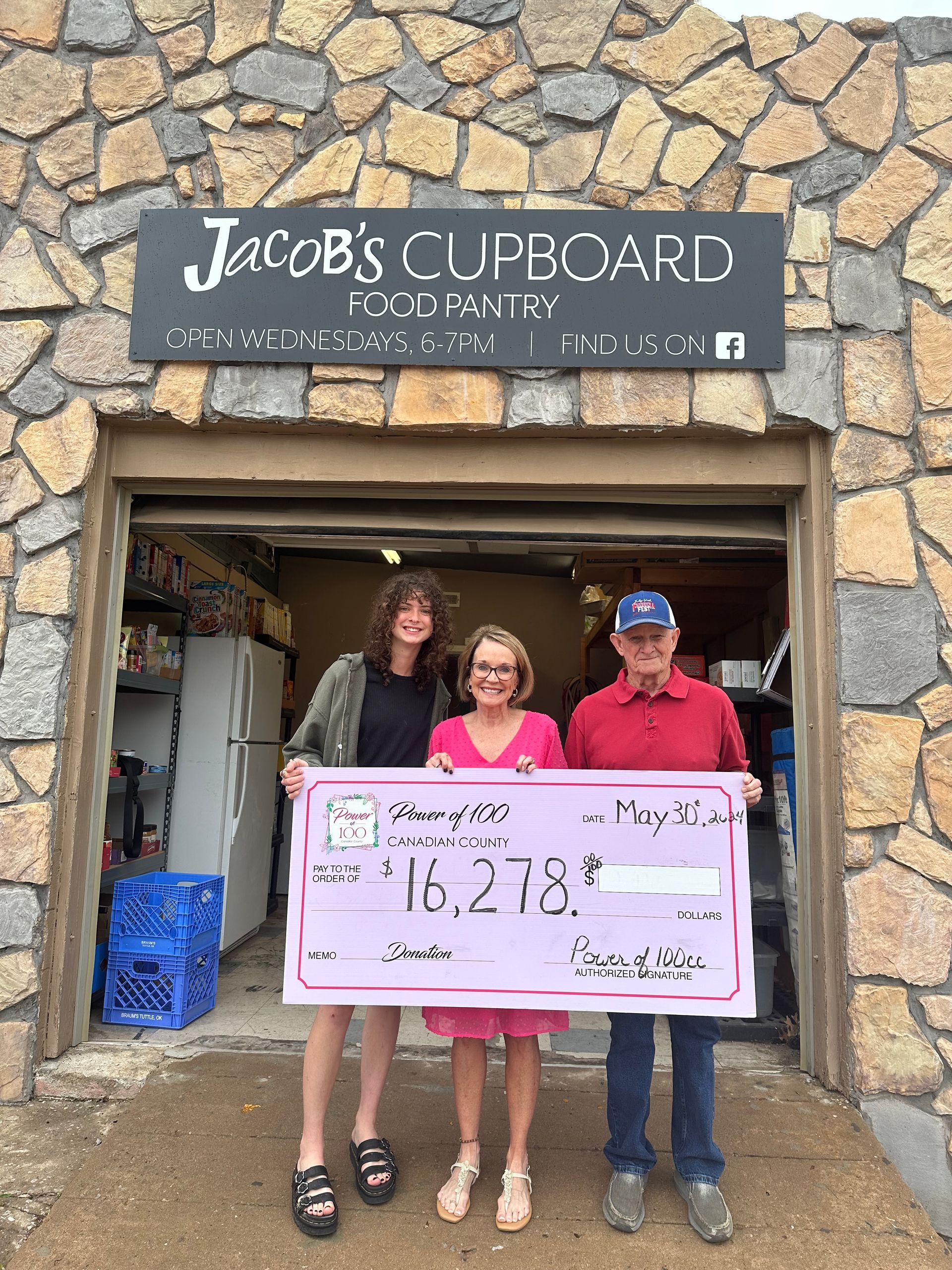 Three people are standing in front of jacob 's cupboard holding a check.