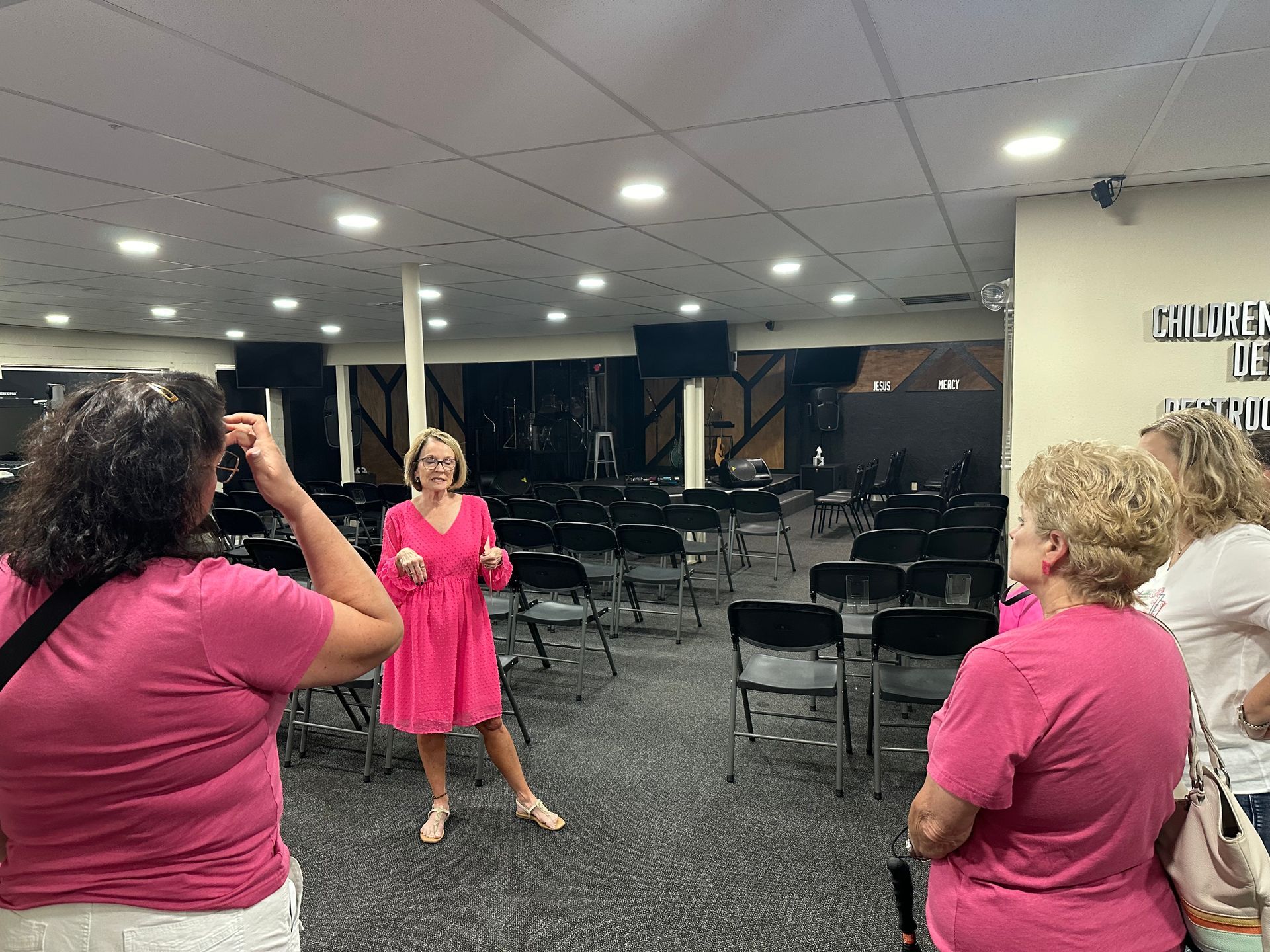 A woman in a pink dress is standing in a room with other women.