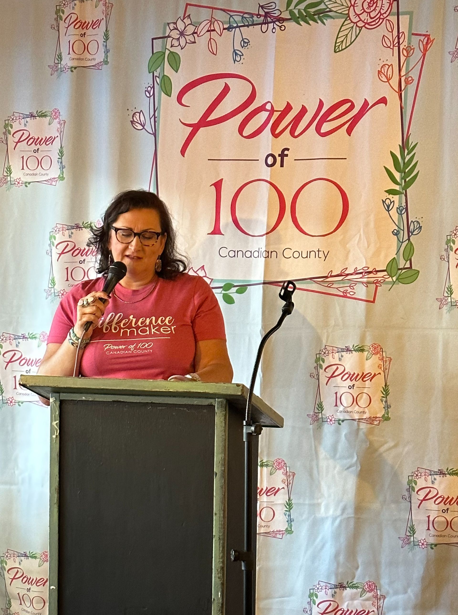 A woman is standing at a podium holding a microphone in front of a sign that says power of 100.