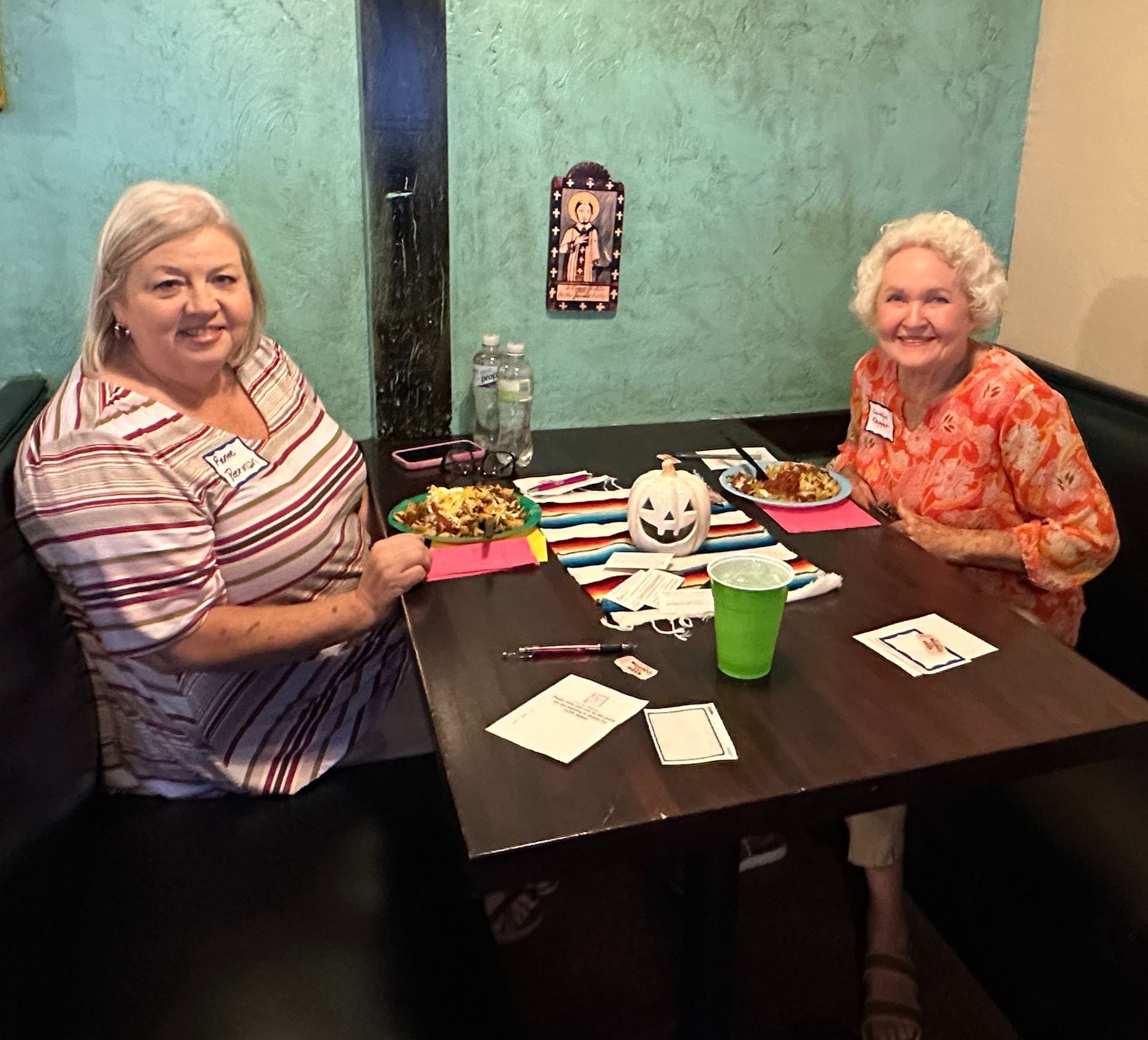 Two women are sitting at a table with a pumpkin on it.