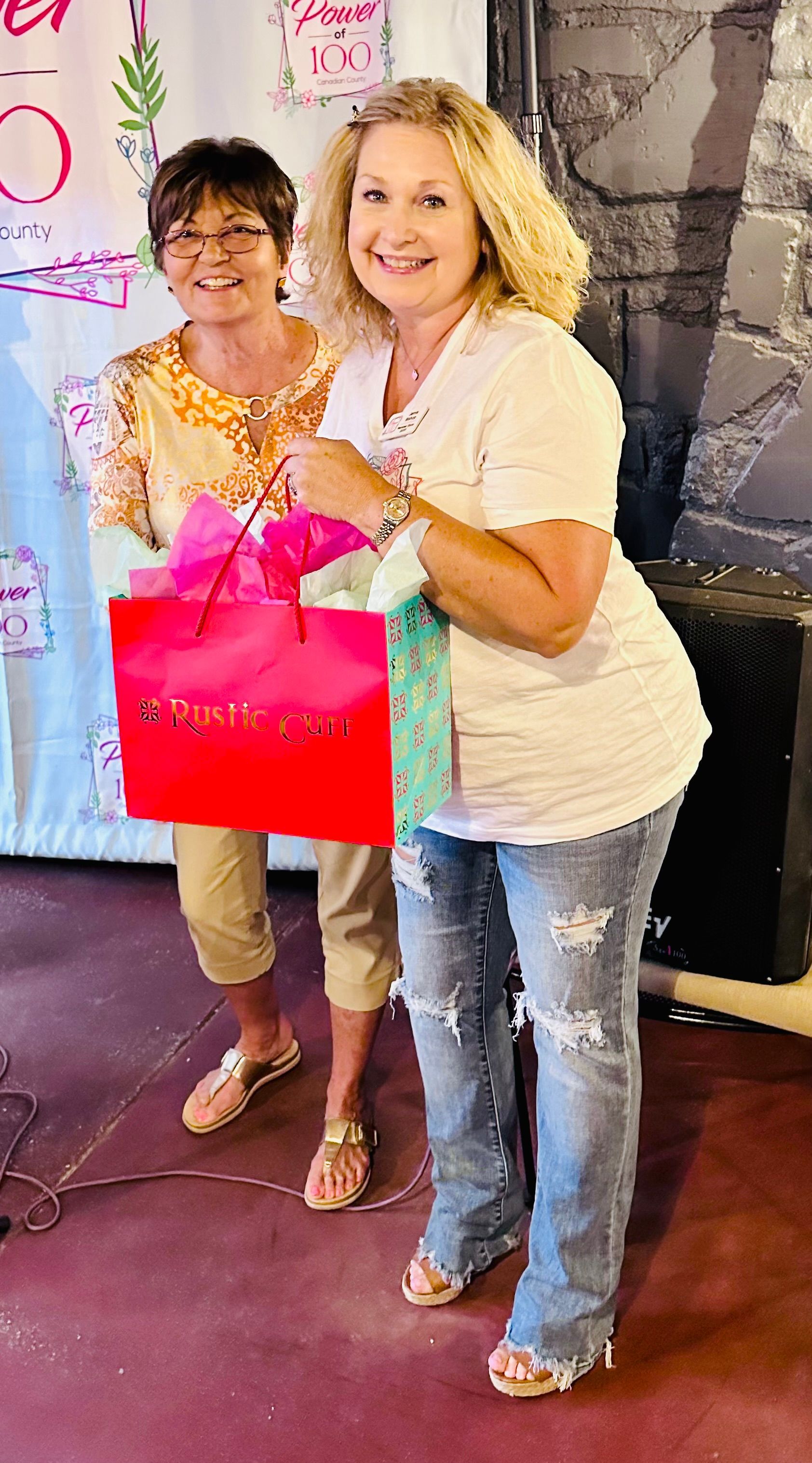 Two women are standing next to each other holding gift bags.