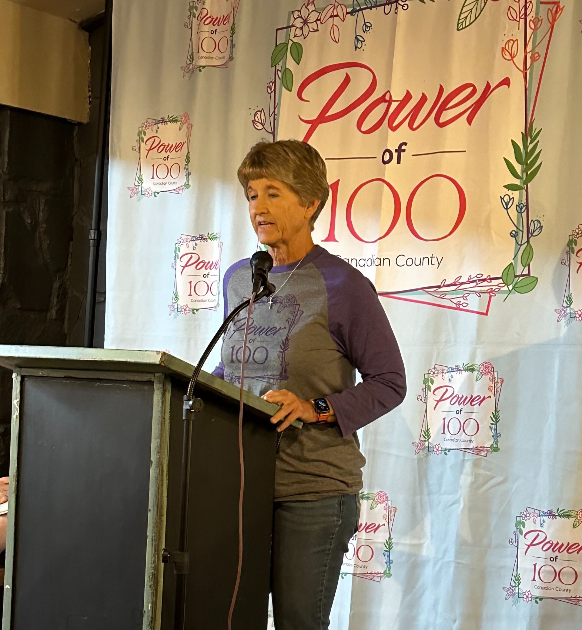 A woman is standing at a podium in front of a power of 100 sign.