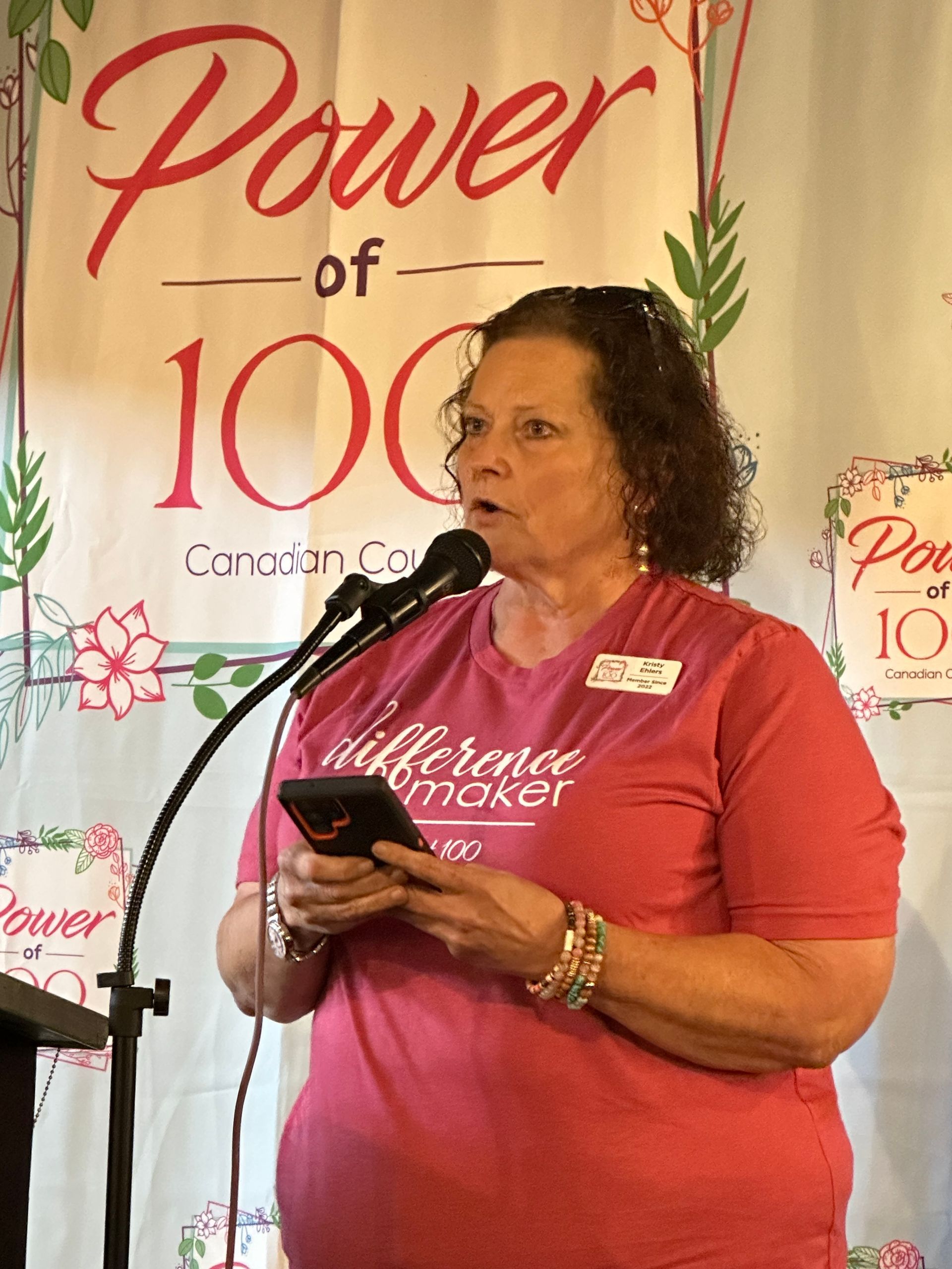 A woman is standing in front of a microphone holding a cell phone.
