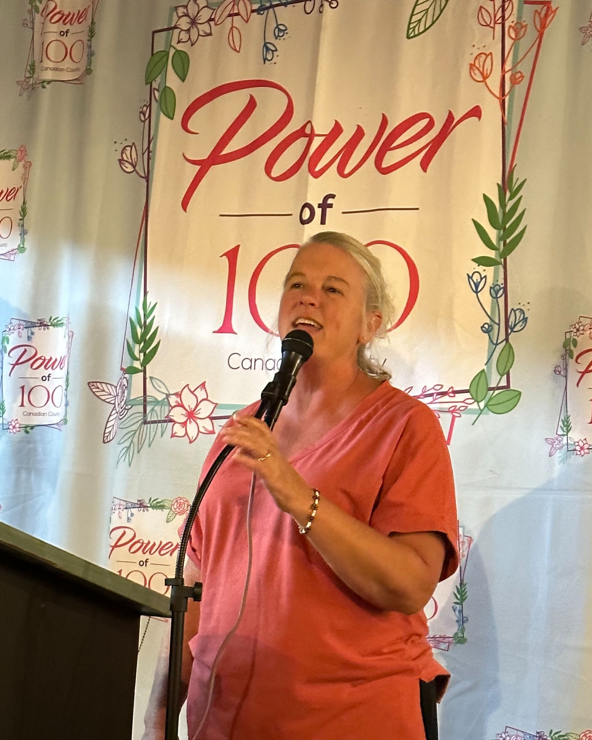 A woman is speaking into a microphone in front of a power of 100 sign.