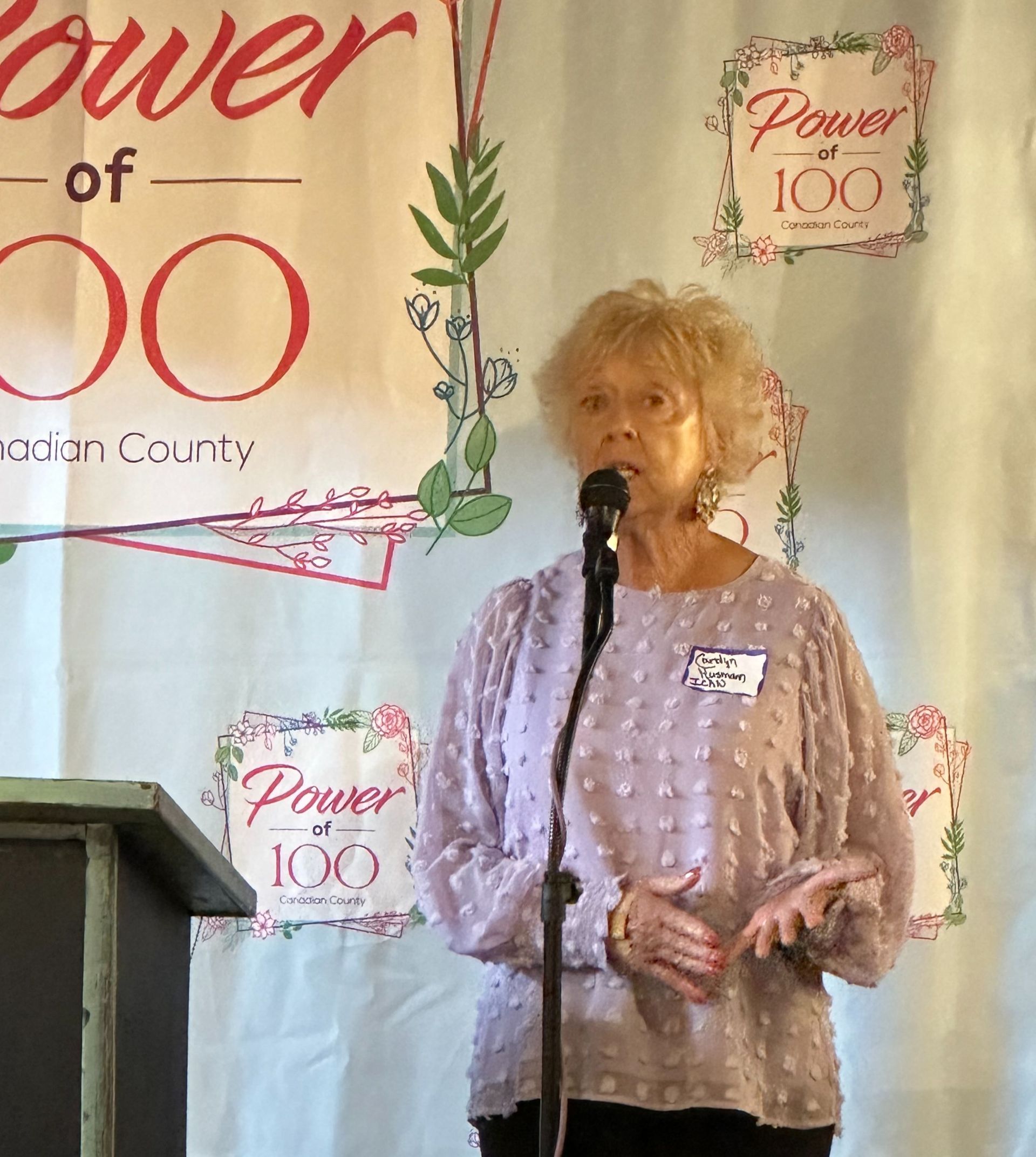 A woman is speaking into a microphone in front of a banner that says power 100