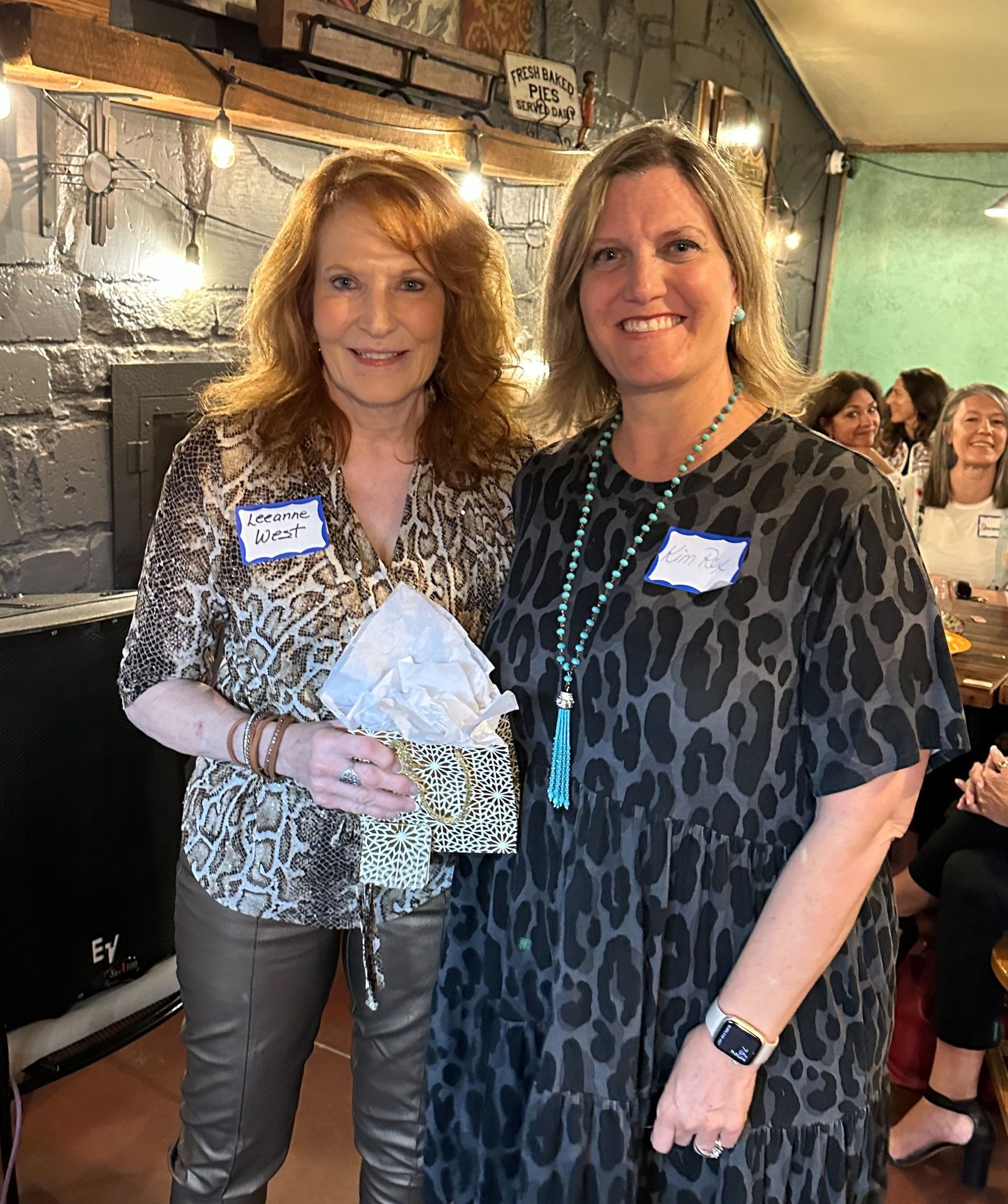 Two women are standing next to each other in a room and smiling.