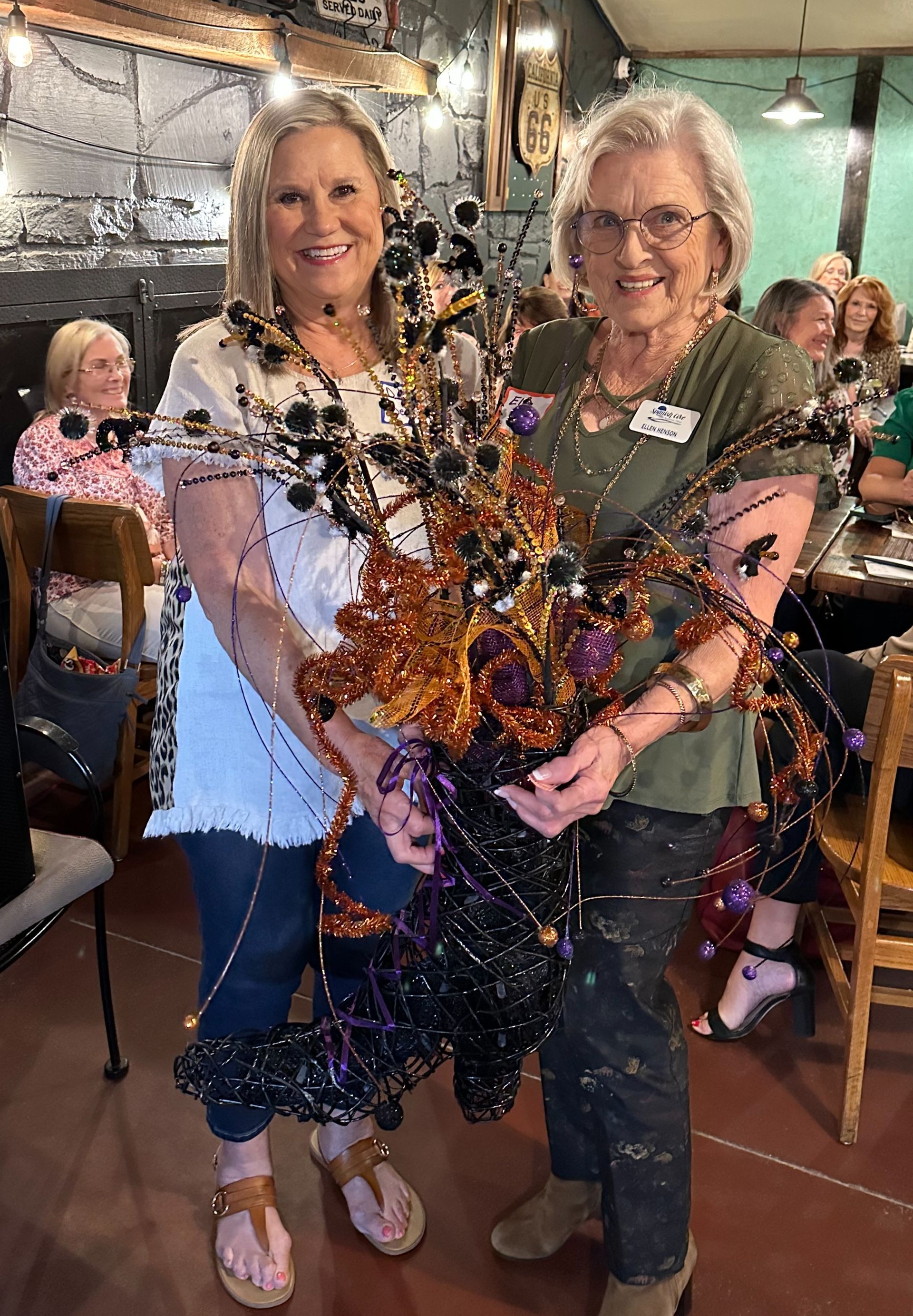 Two women are standing next to each other in a restaurant holding a giant spider.