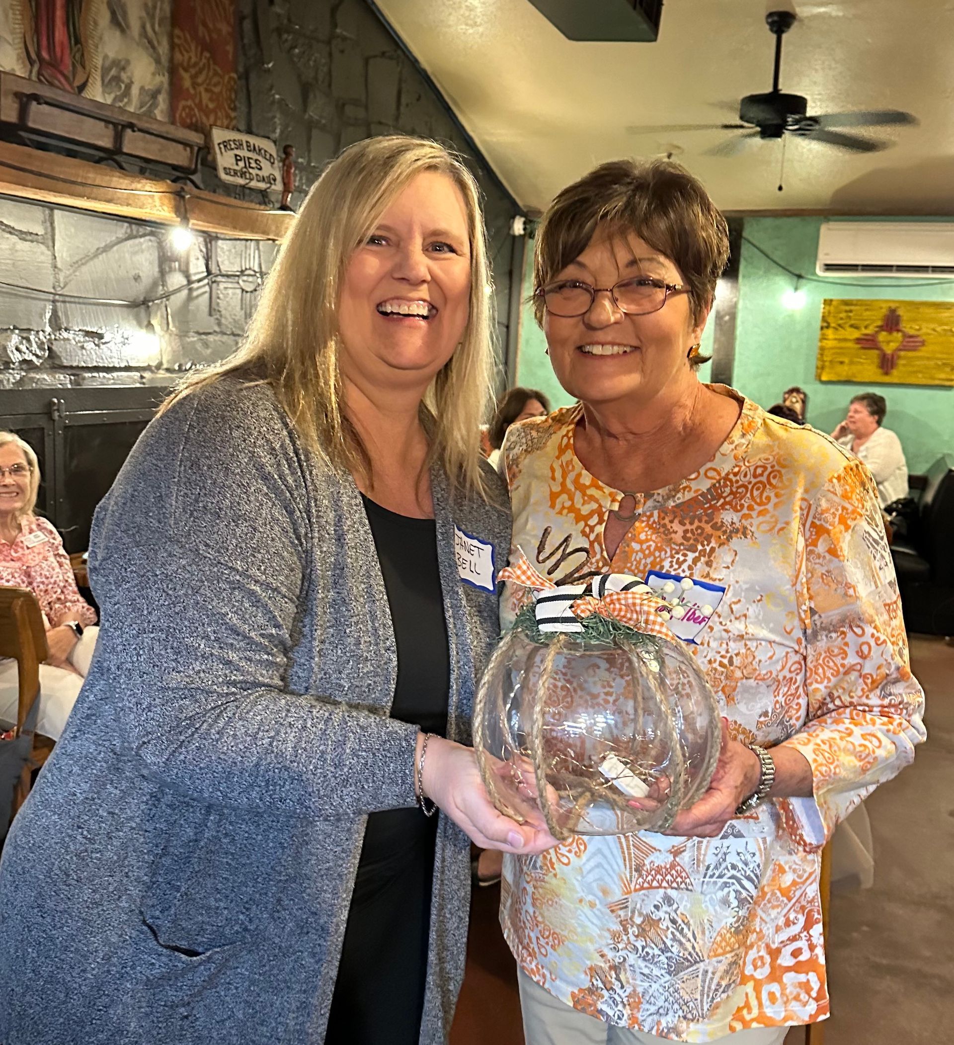 Two women are standing next to each other in a restaurant holding a pumpkin.