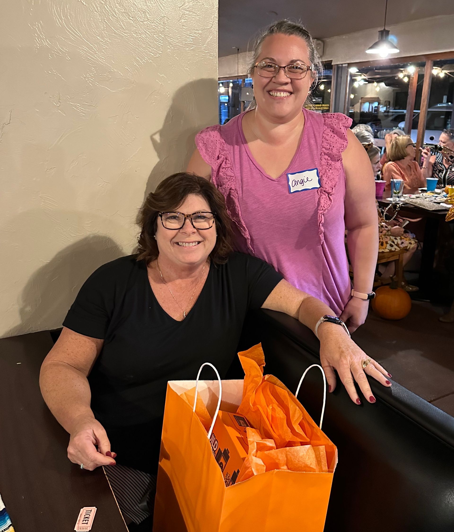 Two women are sitting at a table with a bag of treats.