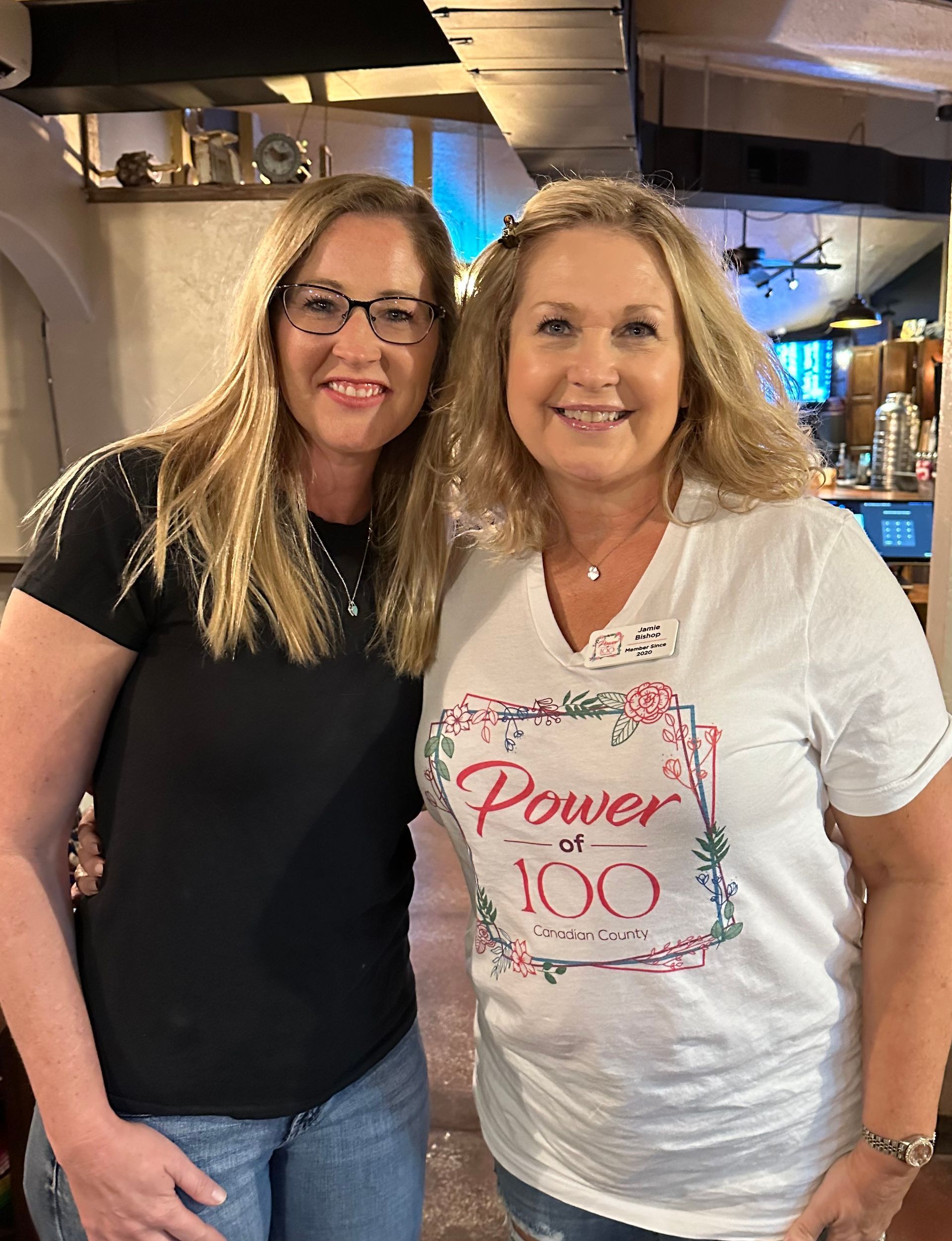 Two women are posing for a picture together and one of them is wearing a t-shirt that says power of 100.