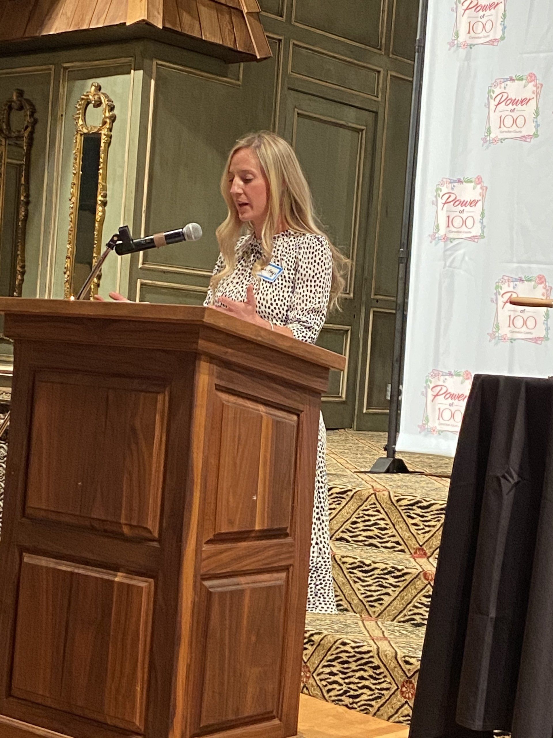 A woman is standing at a wooden podium speaking into a microphone.
