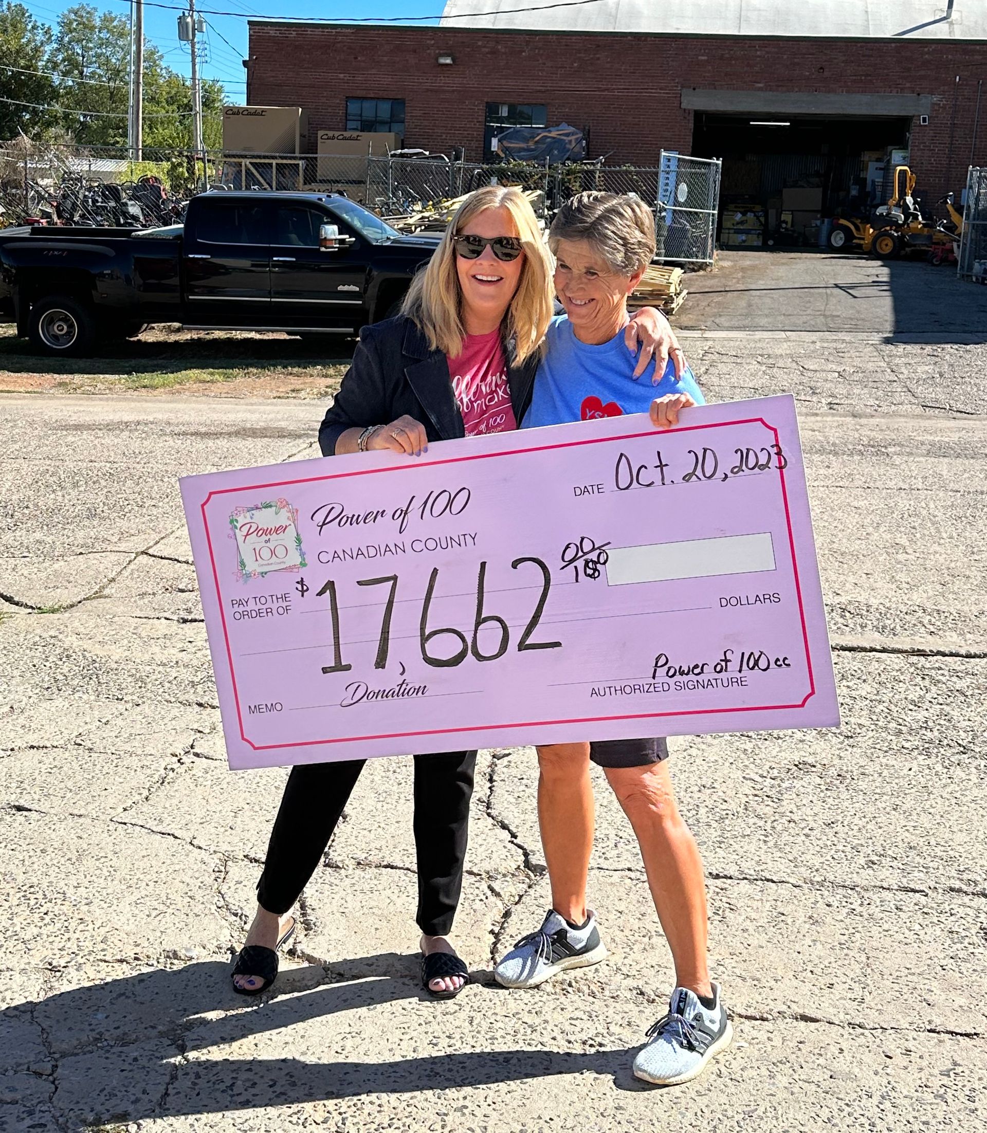 Two women are standing next to each other holding a pink check.