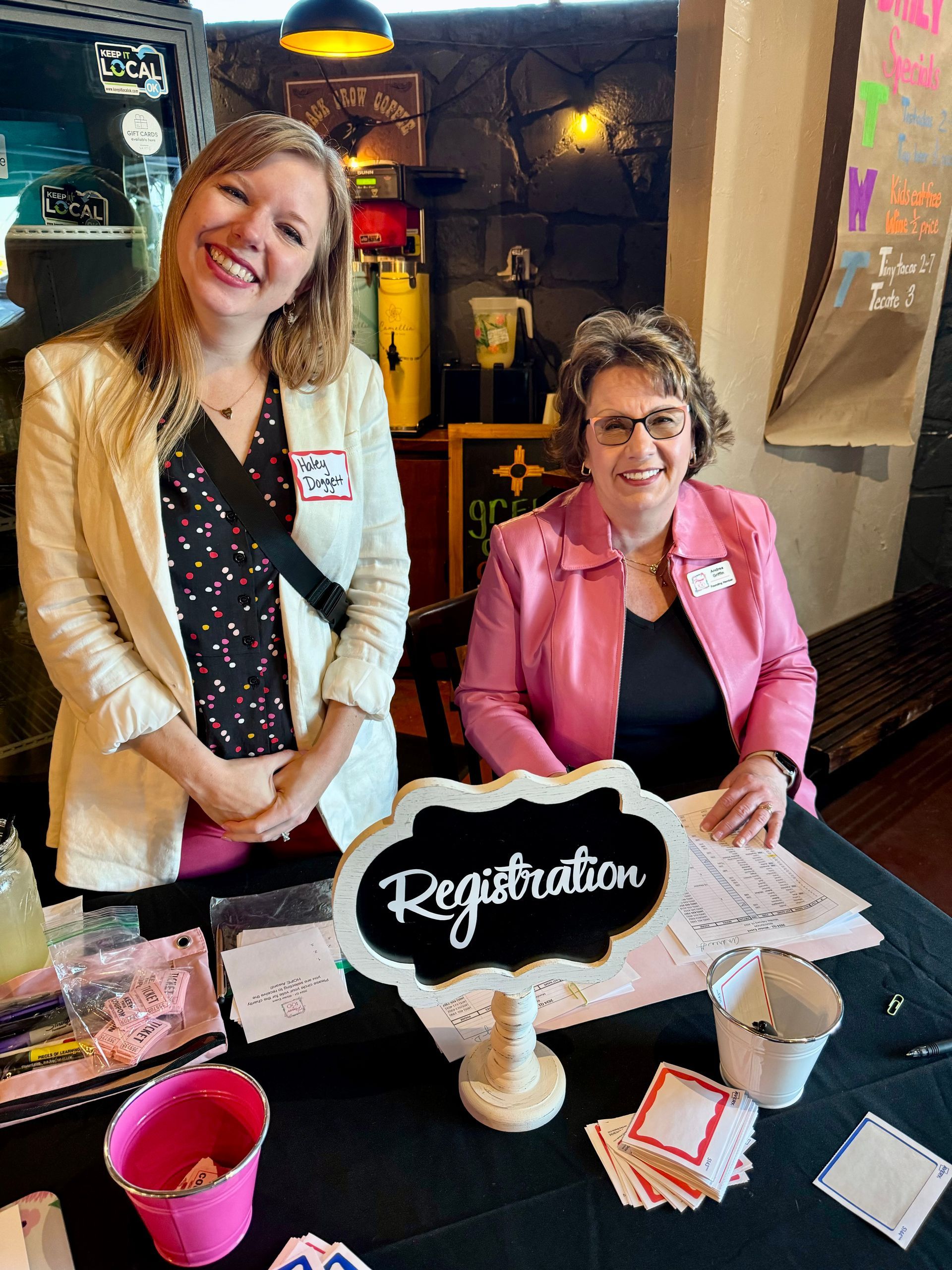 Two women are sitting at a table with a sign that says registration.