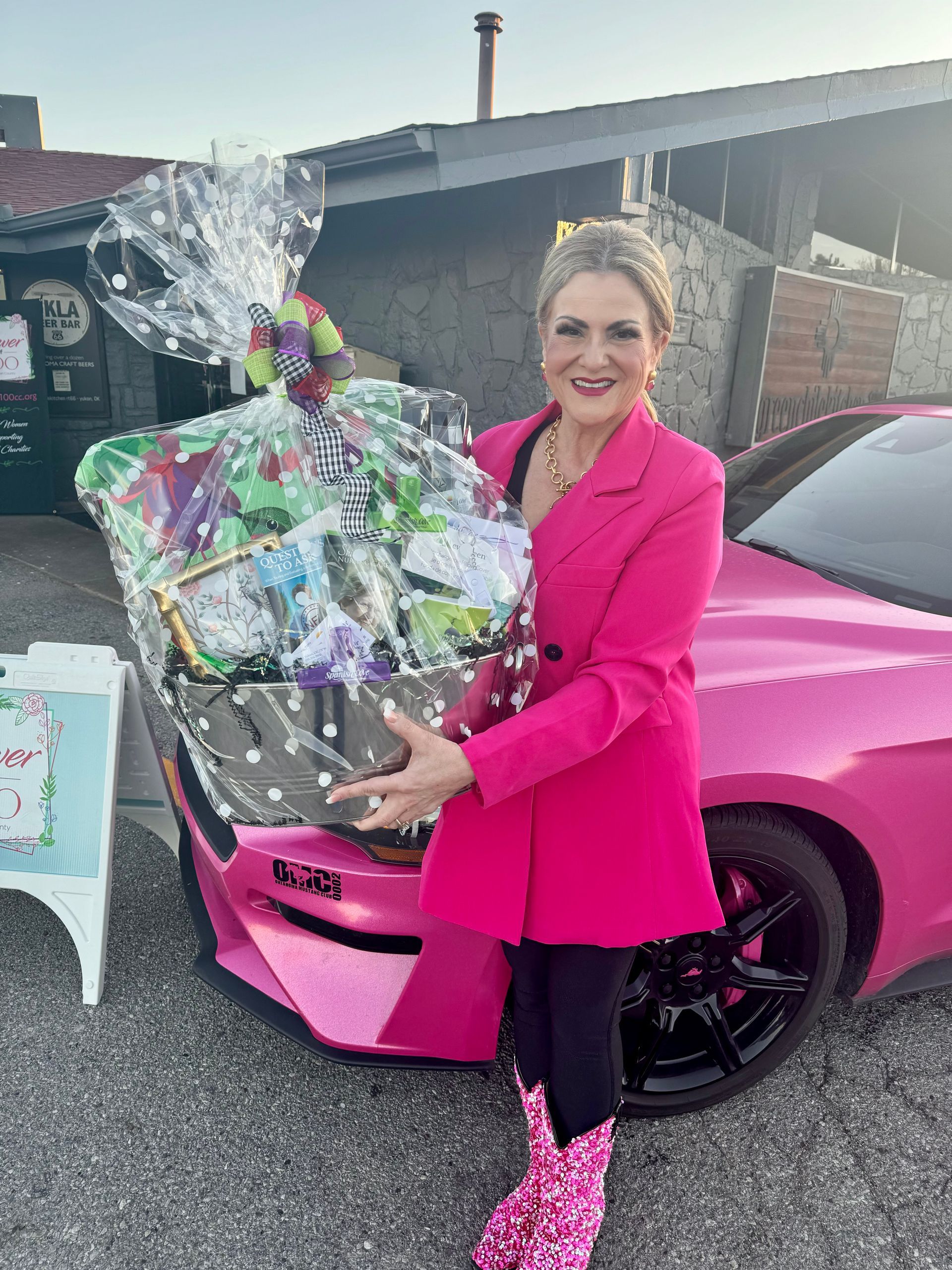 A woman in a pink coat is holding a basket in front of a pink car.