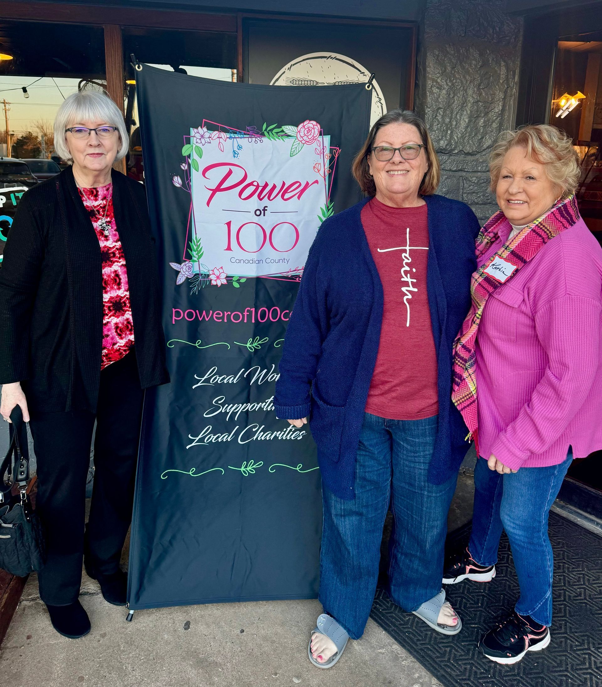 Three women standing in front of a sign that says power over 100