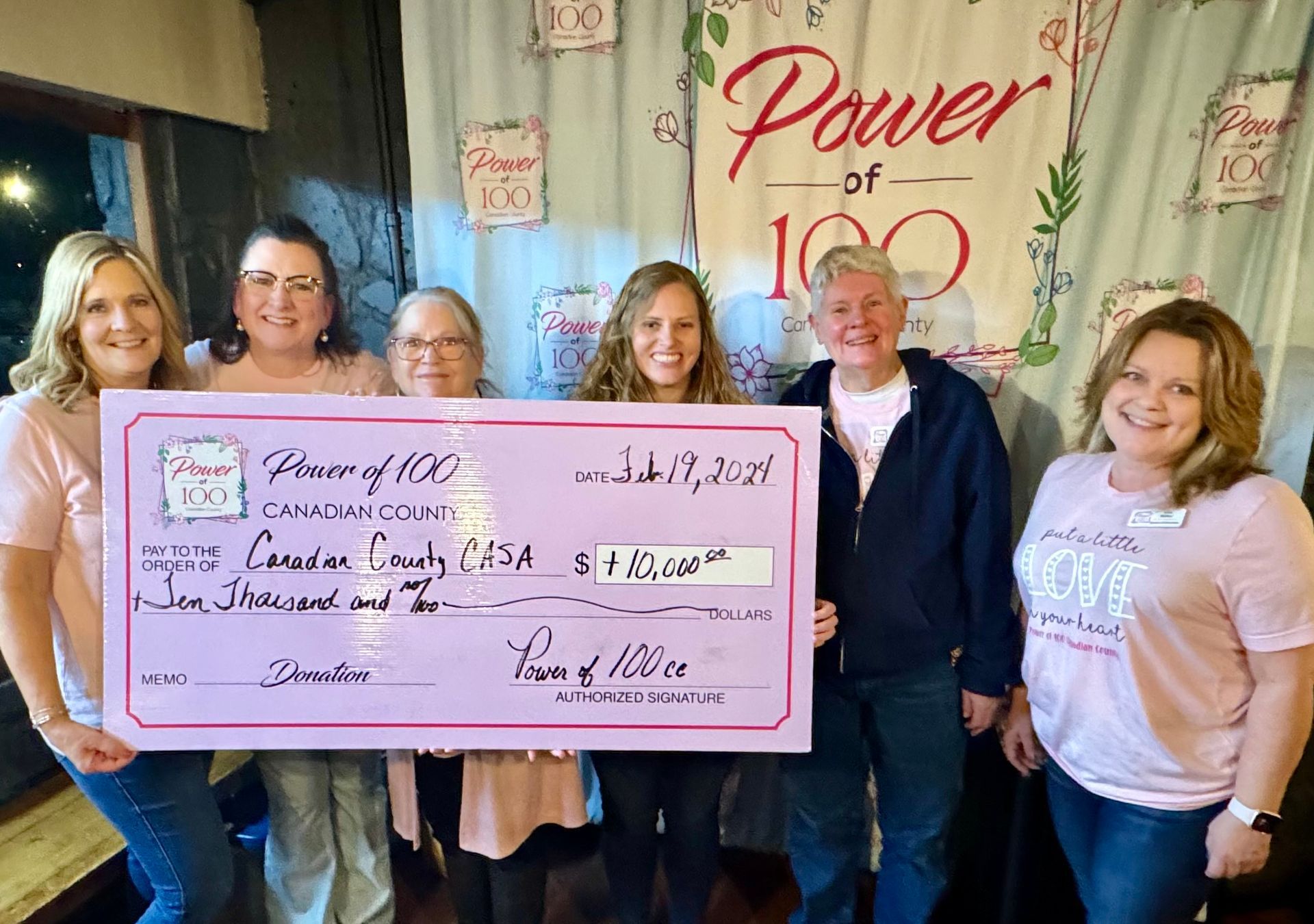 A group of women are holding a large pink check.