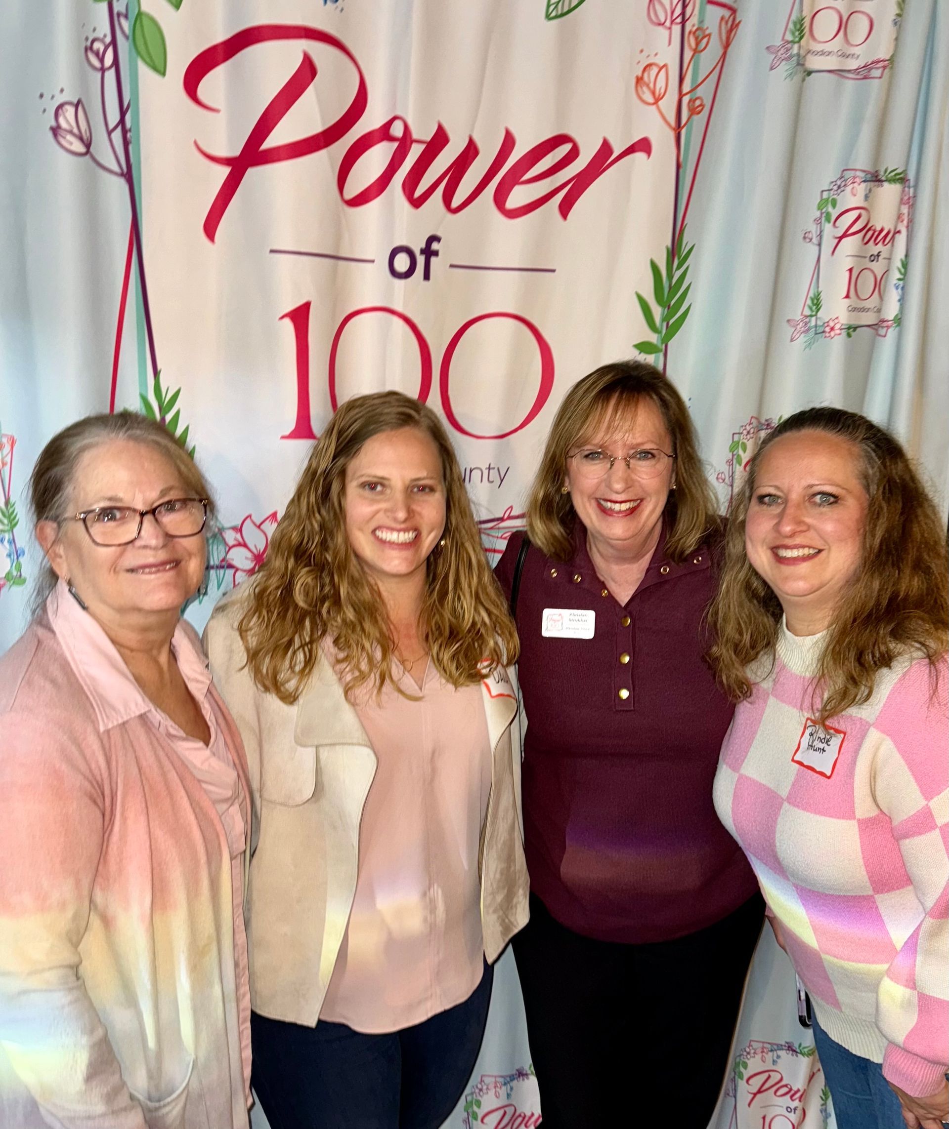 A group of women are posing for a picture in front of a power of 100 sign.