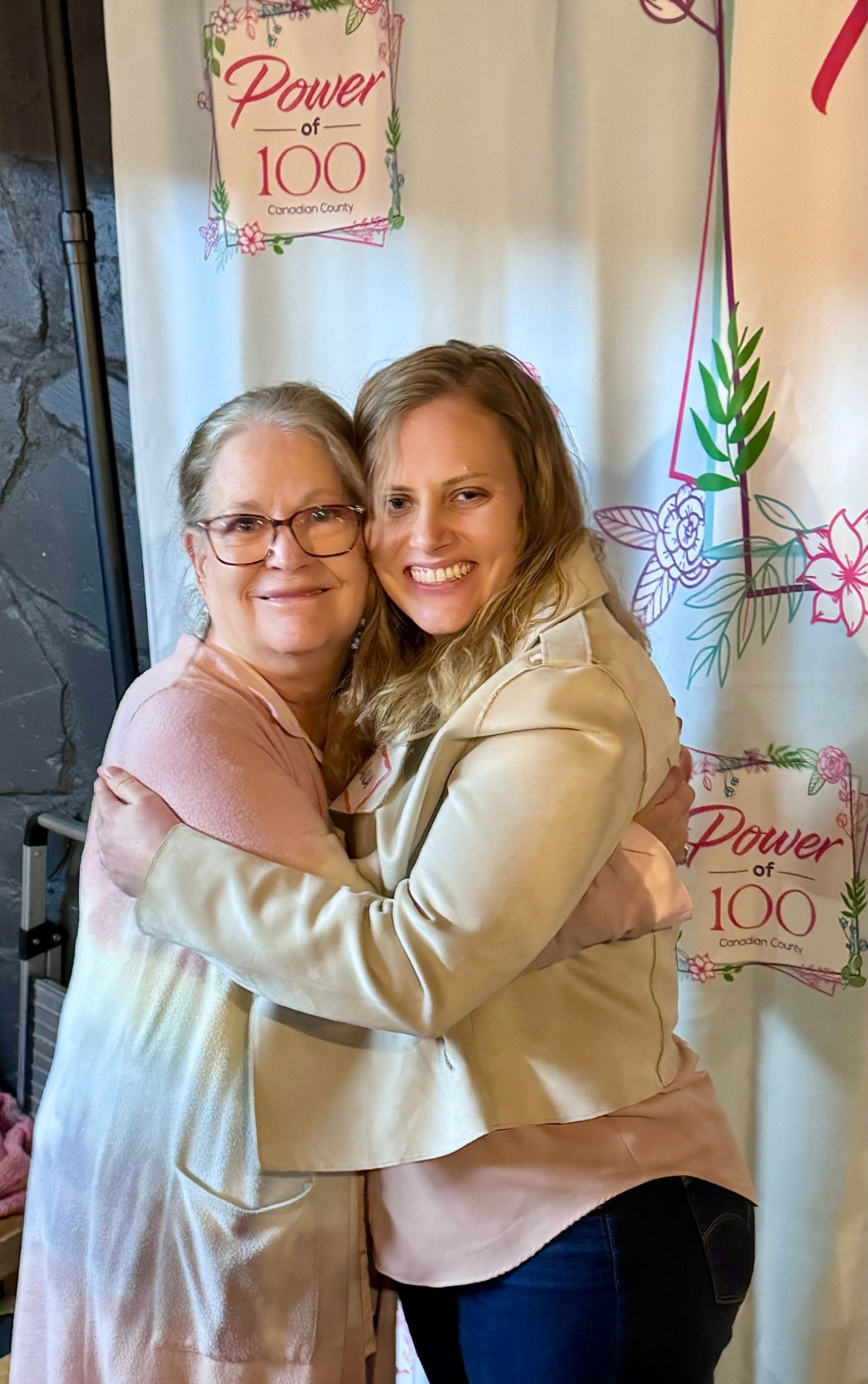 Two women are hugging each other in front of a sign that says prayer 100.