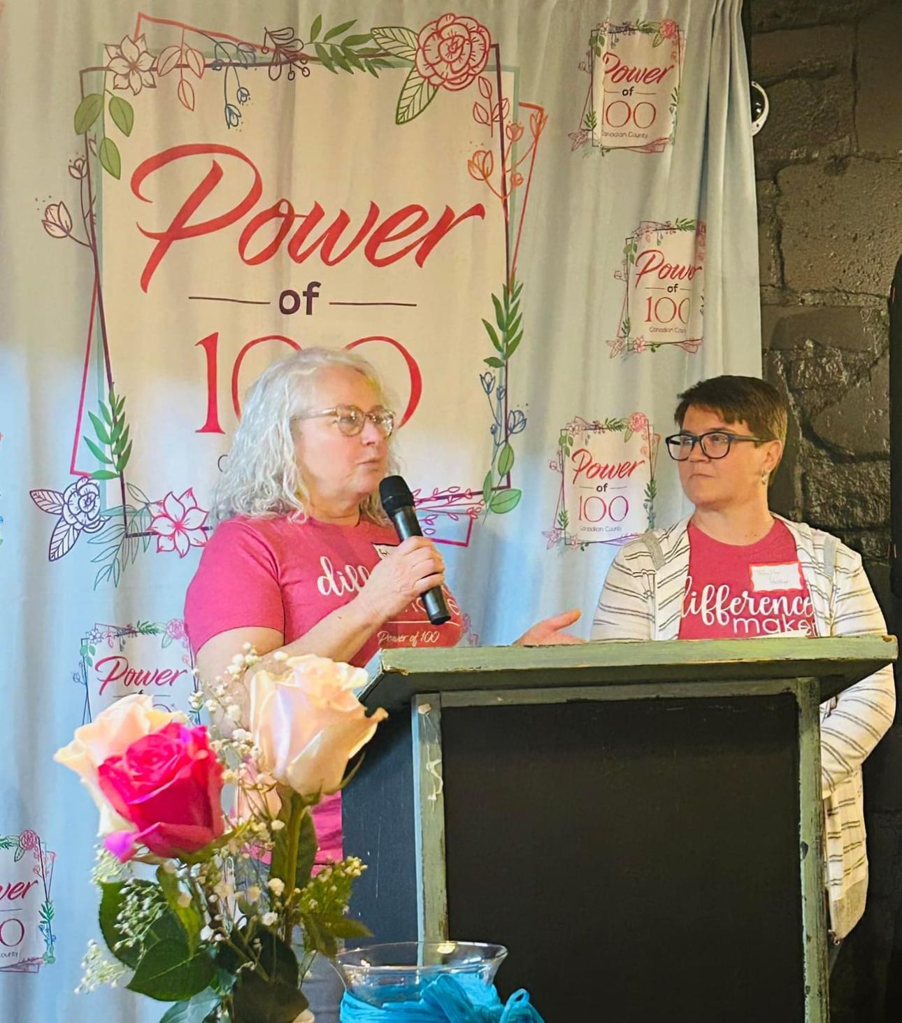 A woman is giving a speech at a podium in front of a sign that says power of 100