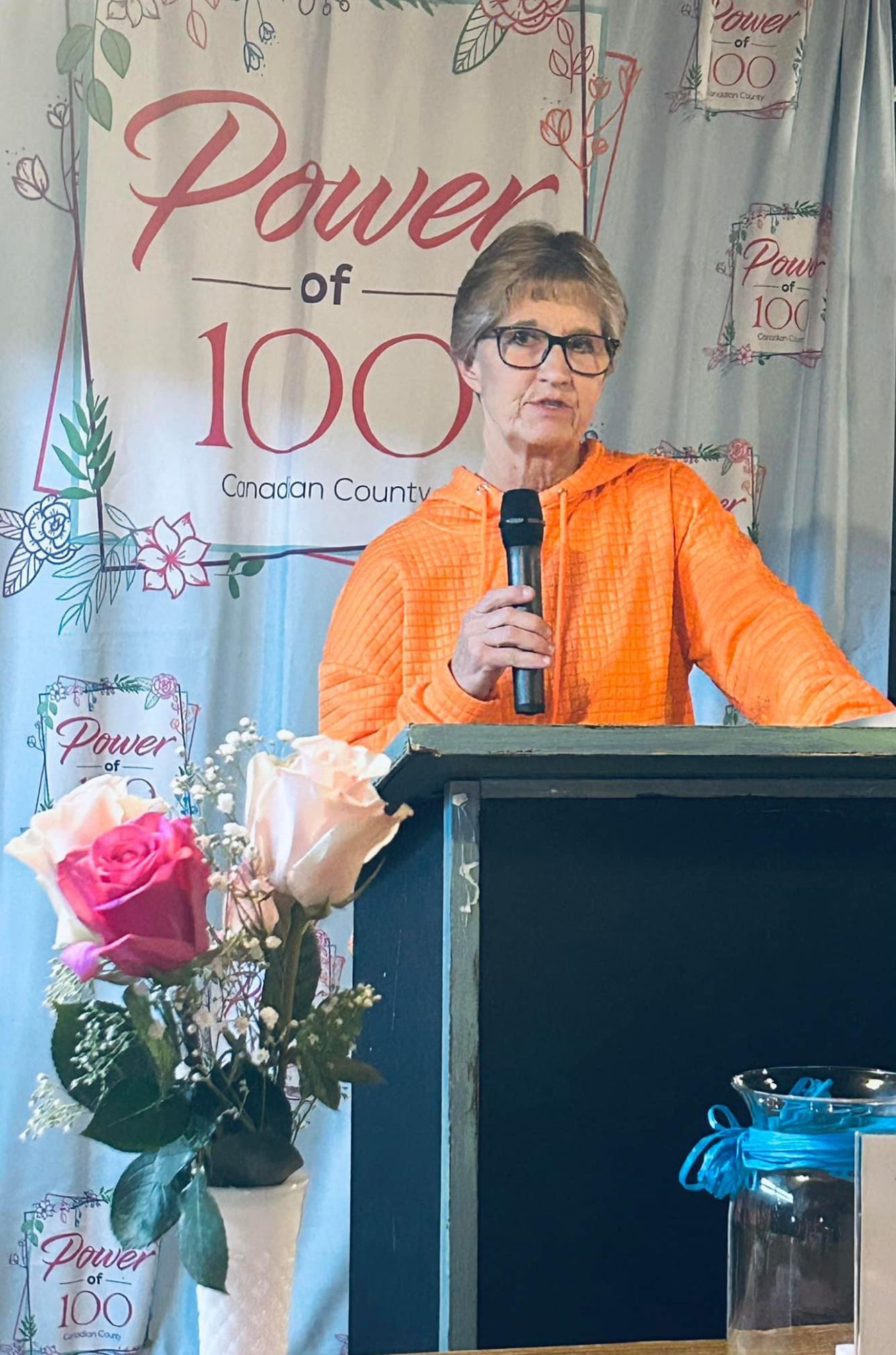A woman is standing at a podium holding a microphone.