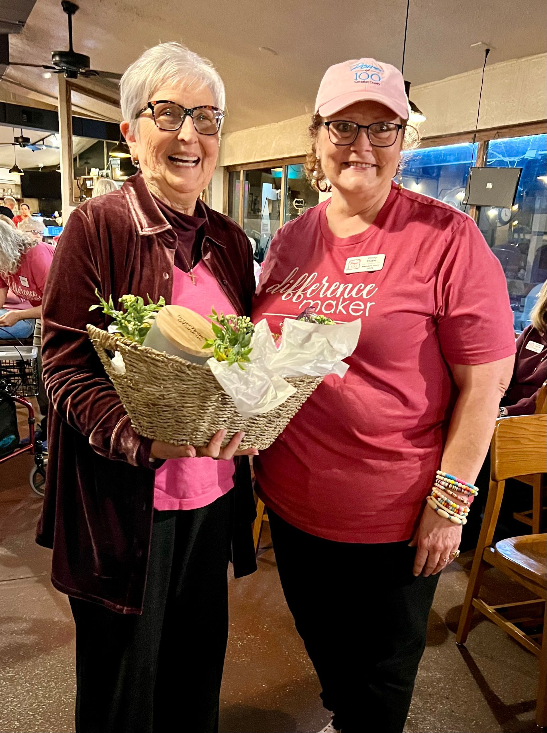 Two women are standing next to each other holding a basket of food.