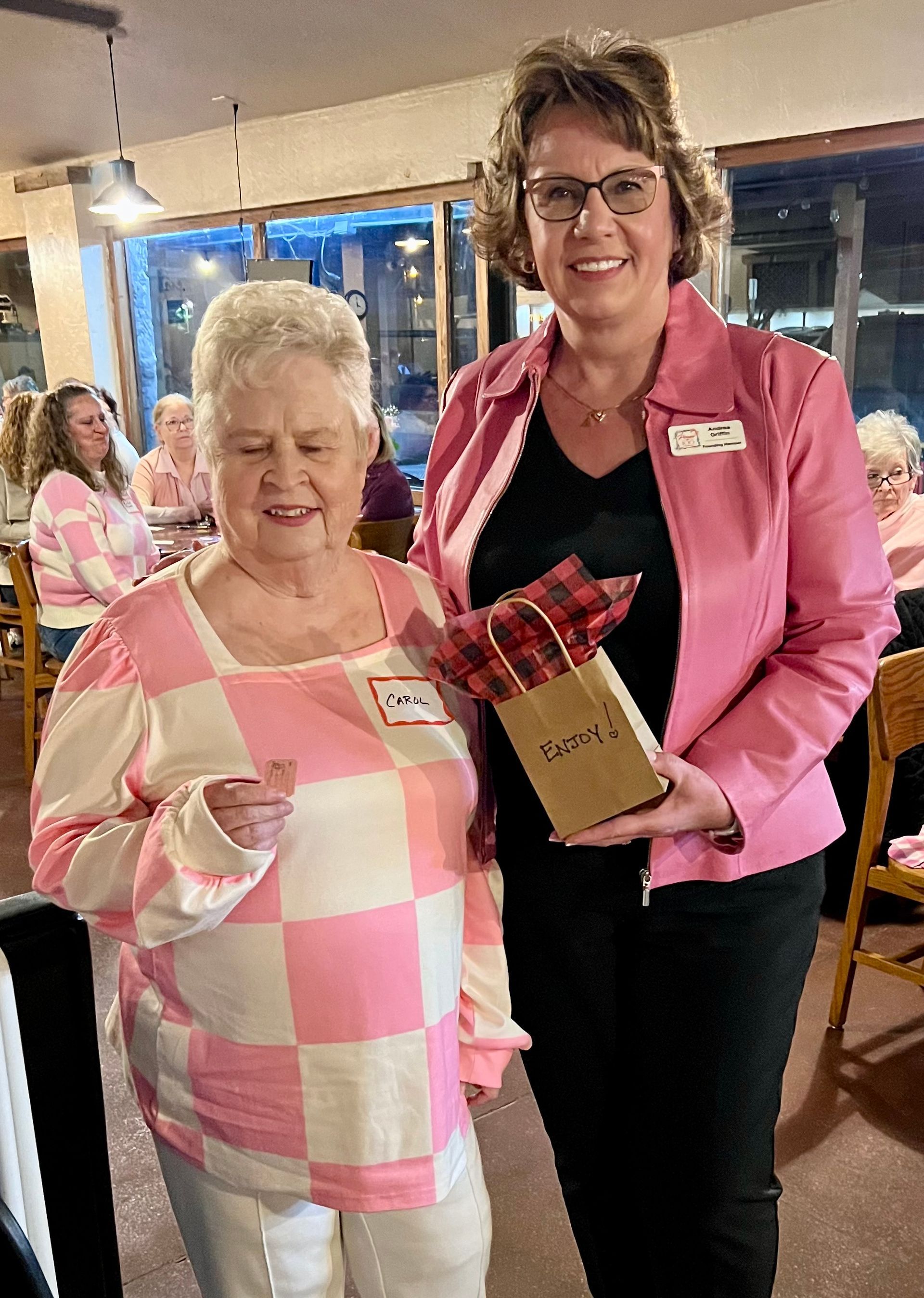 Two women are standing next to each other in a room . one of the women is wearing a pink jacket.