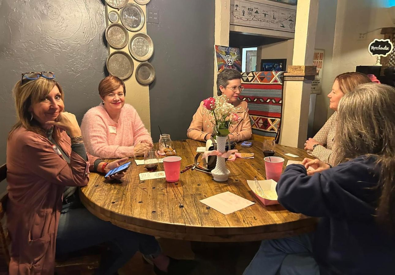 A group of women are sitting around a wooden table.