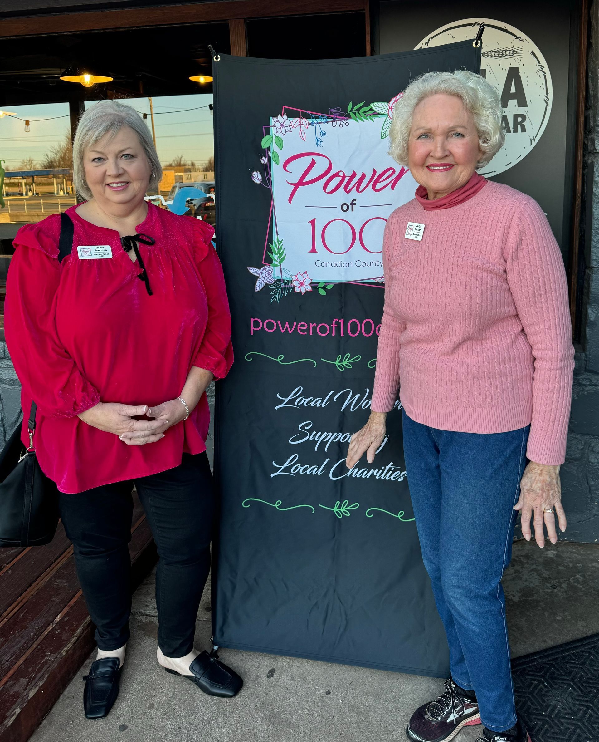 Two women are standing next to each other in front of a sign that says power at 100.
