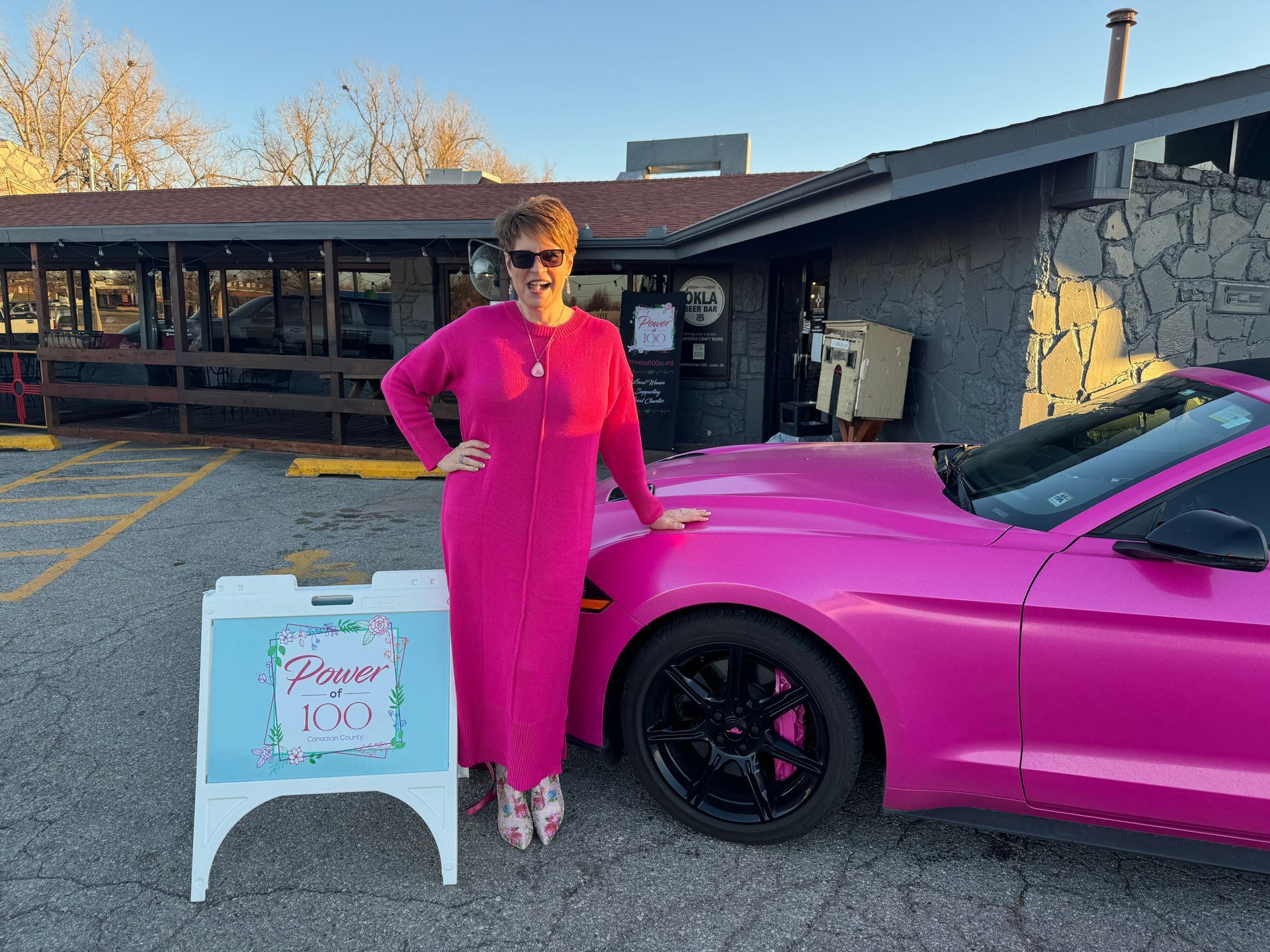 A woman in a pink dress is standing next to a pink car.
