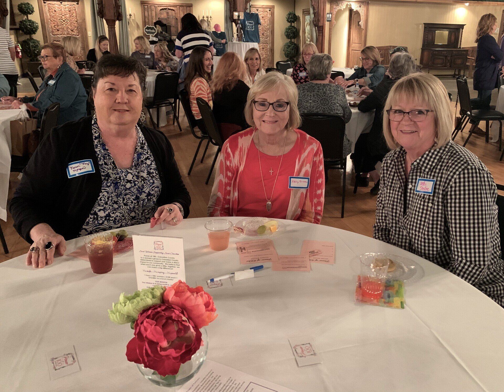Three women are sitting at a table with flowers on it.