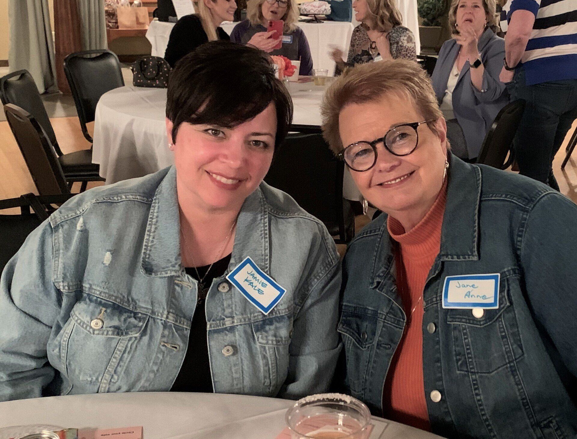 Two women are posing for a picture while sitting at a table.