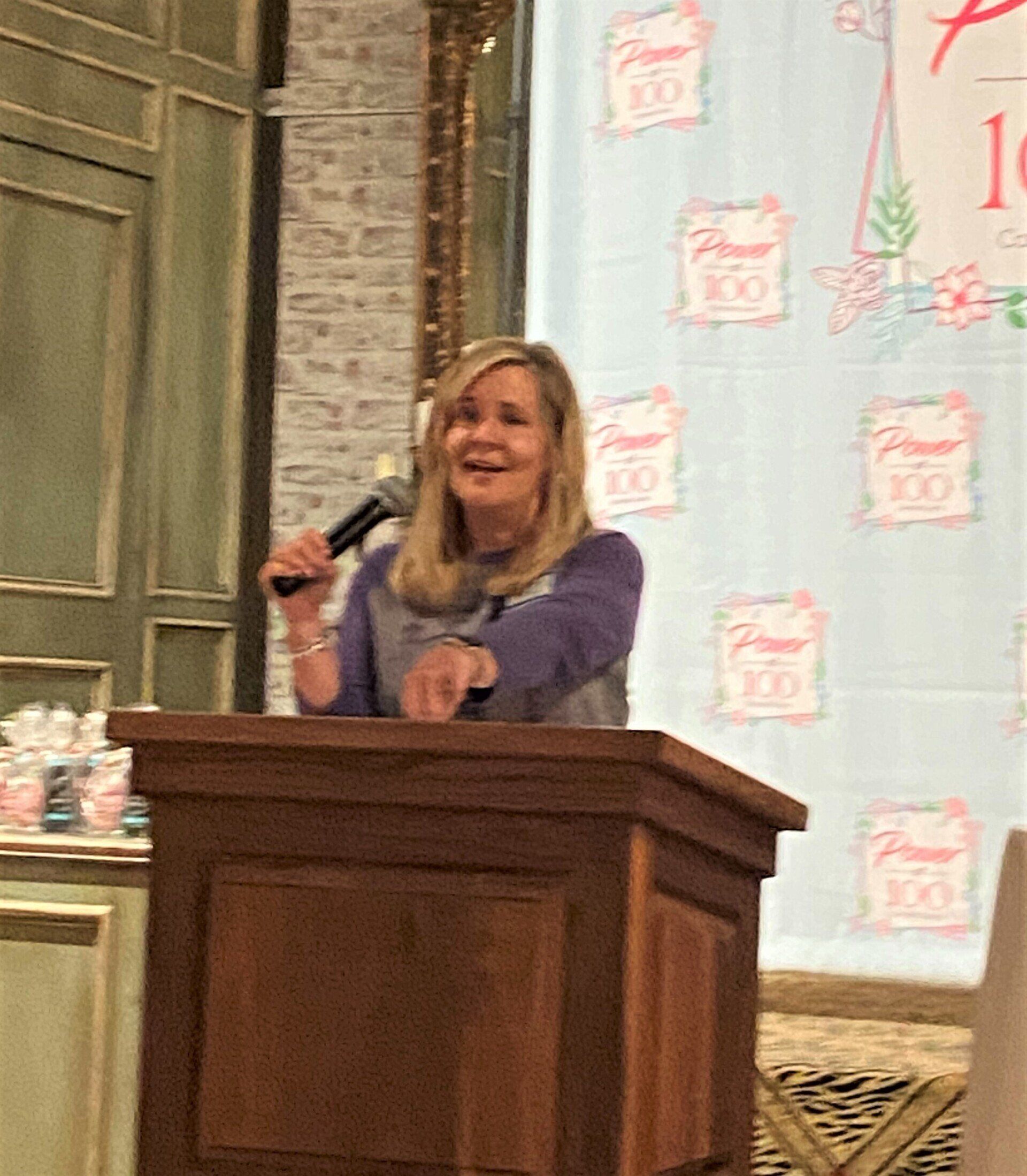 A woman is standing at a podium holding a microphone.