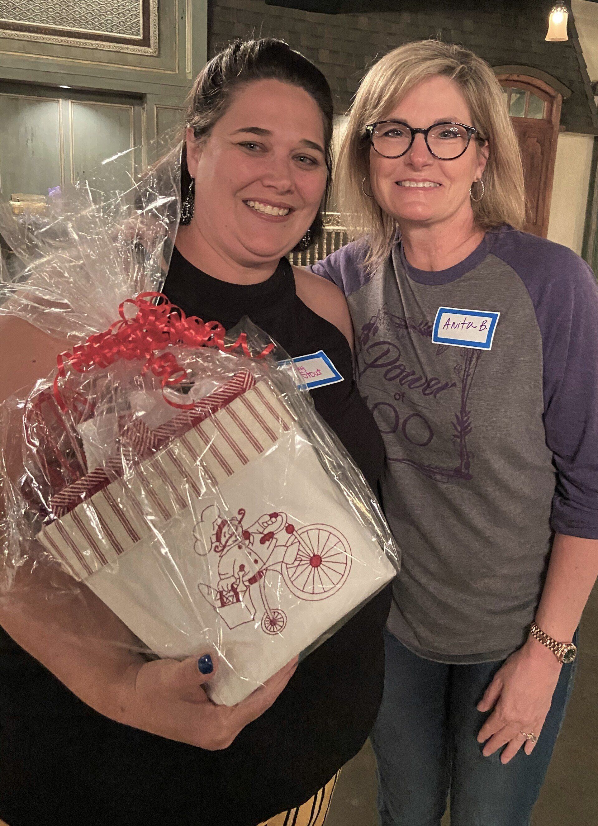Two women are standing next to each other holding a gift basket.